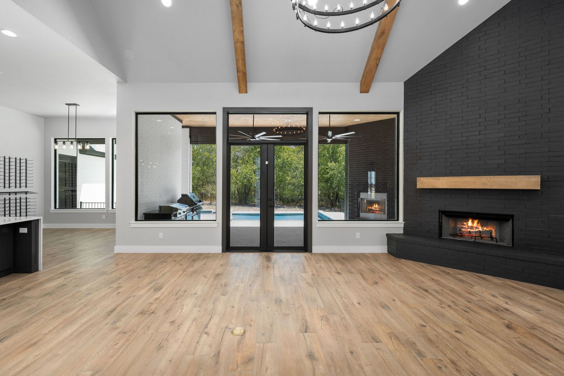 Bright modern living room with wood floors, black fireplace wall, and glass doors to a green view.