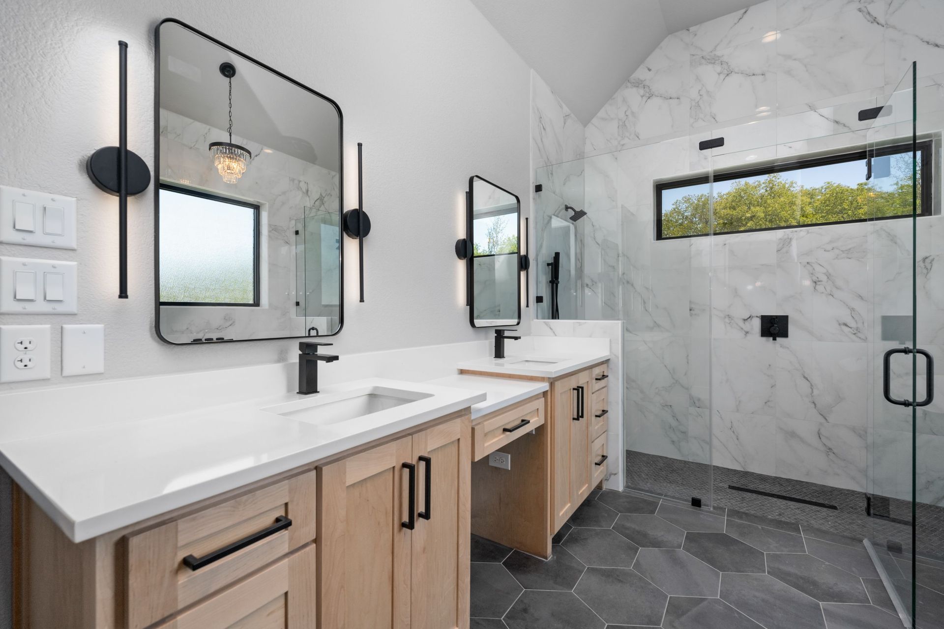 Modern bathroom with double vanity, mirrors, white marble walls, and dark hex tile floor