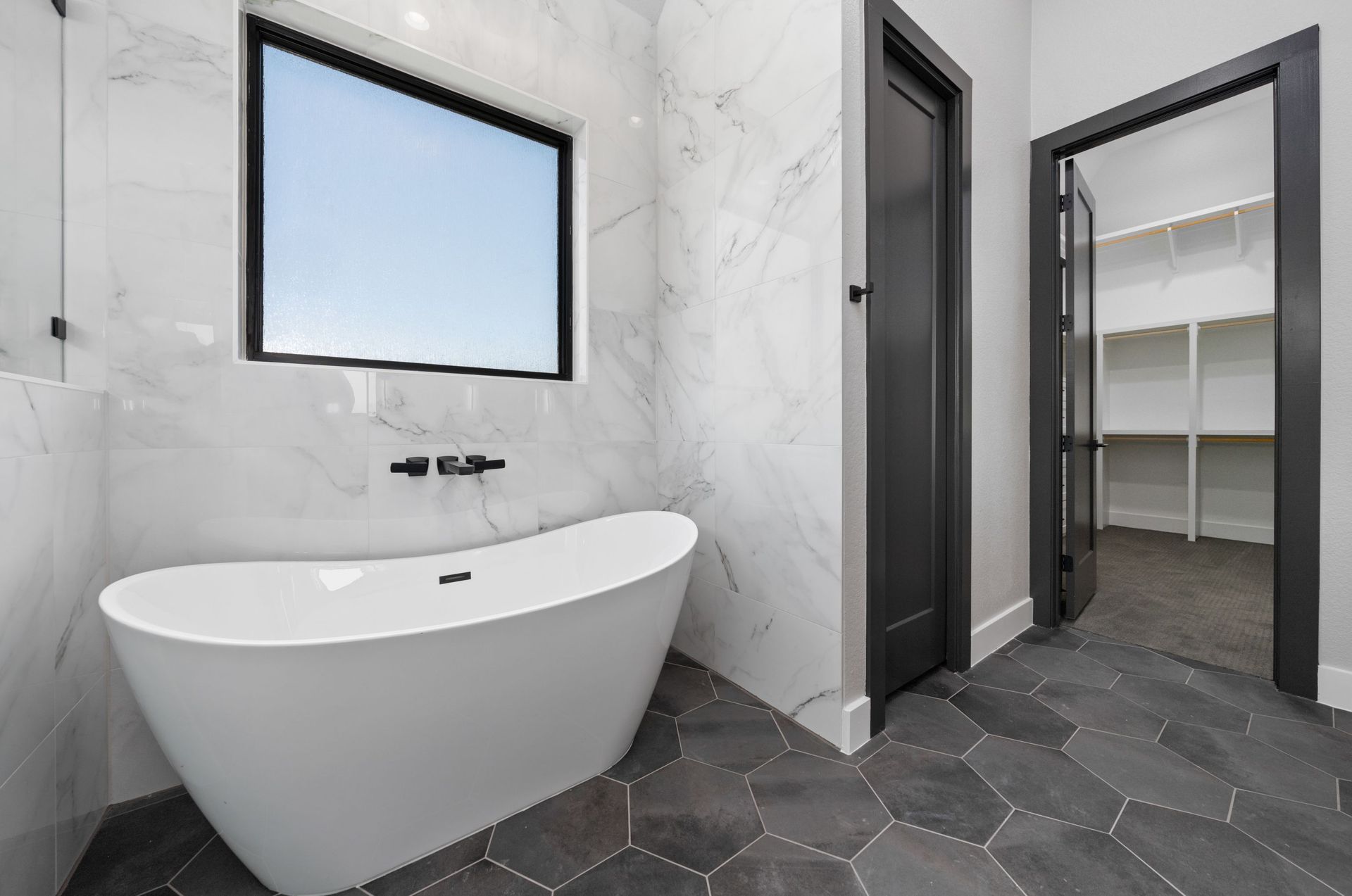 Modern bathroom with freestanding tub, wall mirror, marble tile, and open closet door