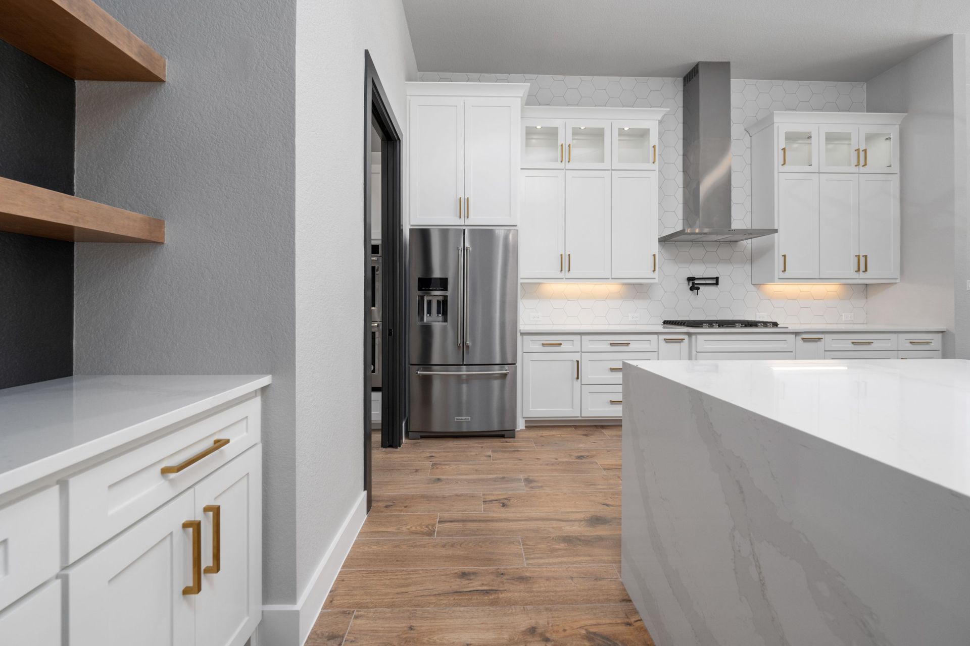 Modern white kitchen with stainless steel fridge, marble island, and wood floors