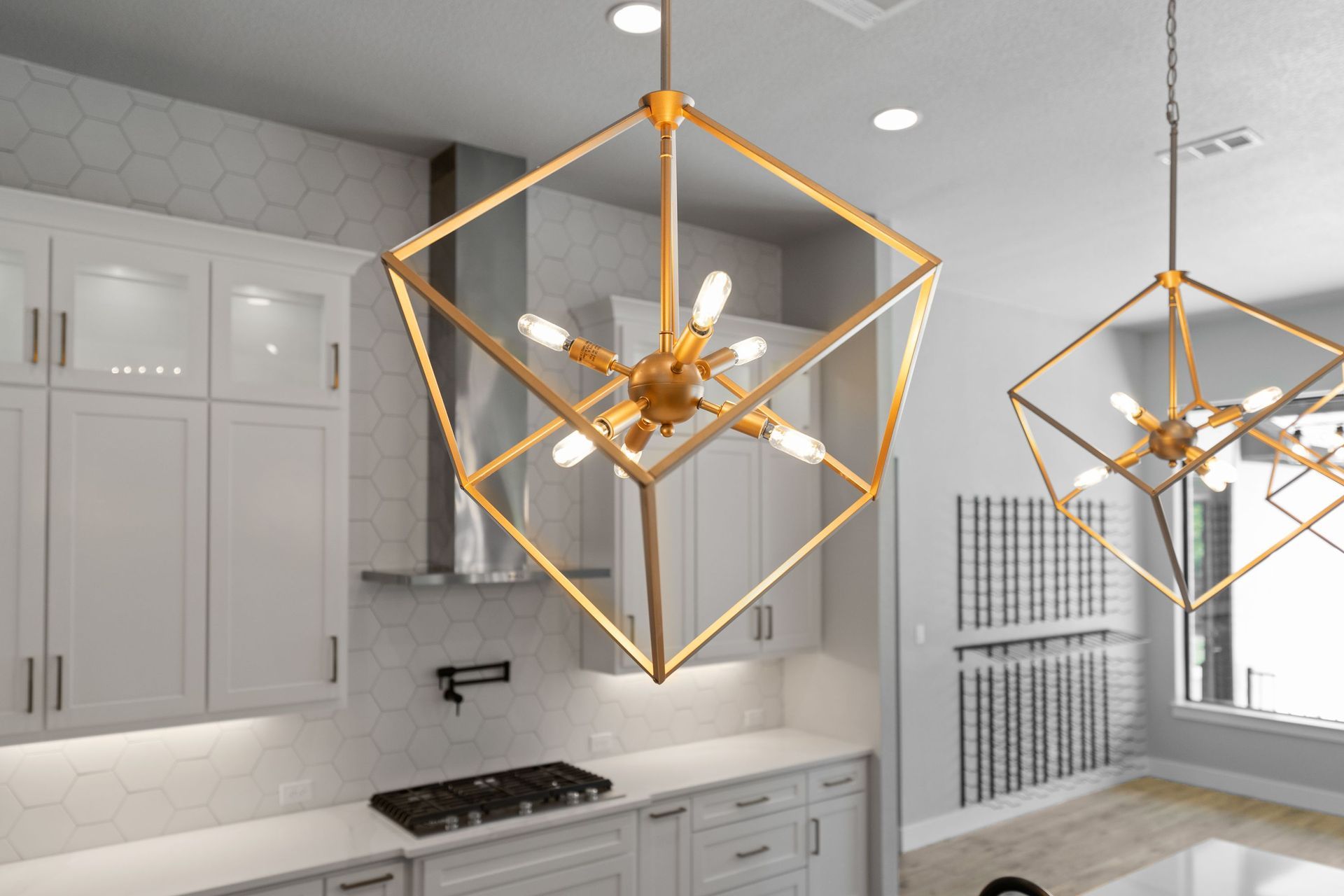 Modern kitchen with white cabinets and gold geometric pendant lights above a gray countertop