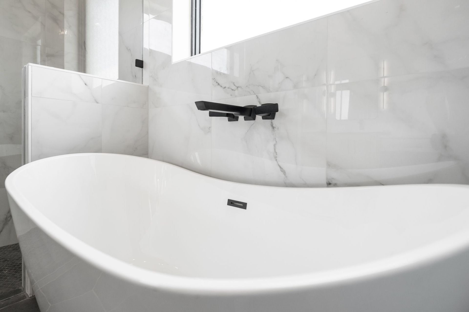Minimalist white bathroom with freestanding tub and wall-mounted black faucet