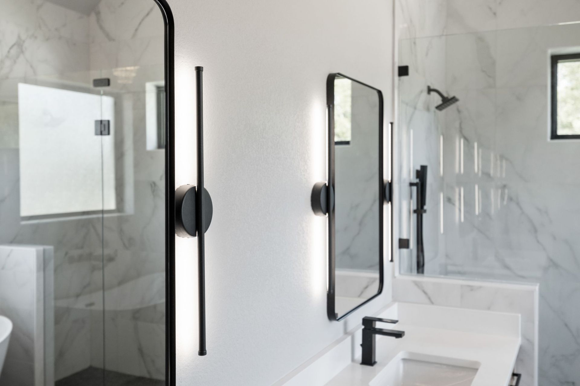 Modern bathroom with glass shower, black-framed mirrors, white vanity, and marble-look walls