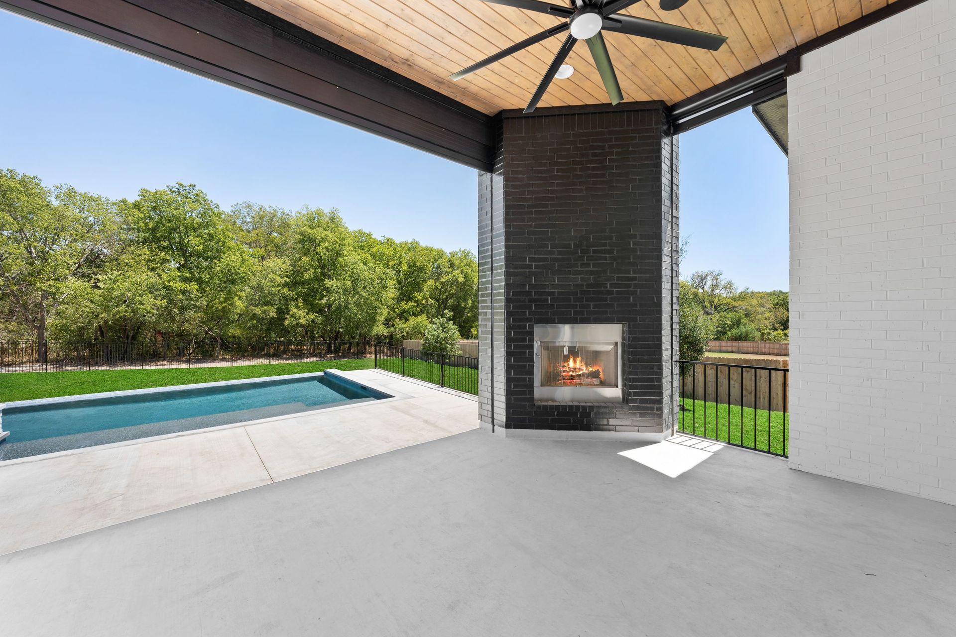 Covered patio with fireplace overlooking a backyard pool and green trees