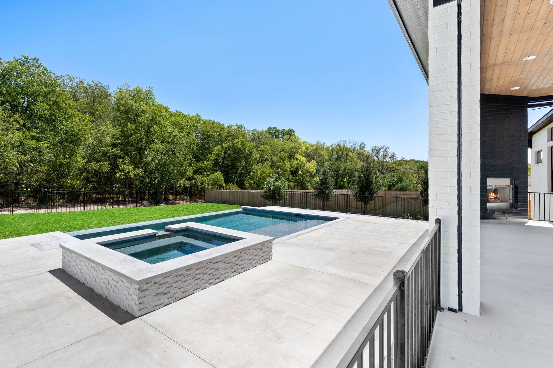 Modern backyard patio with a rectangular pool, concrete deck, and trees beyond the fence