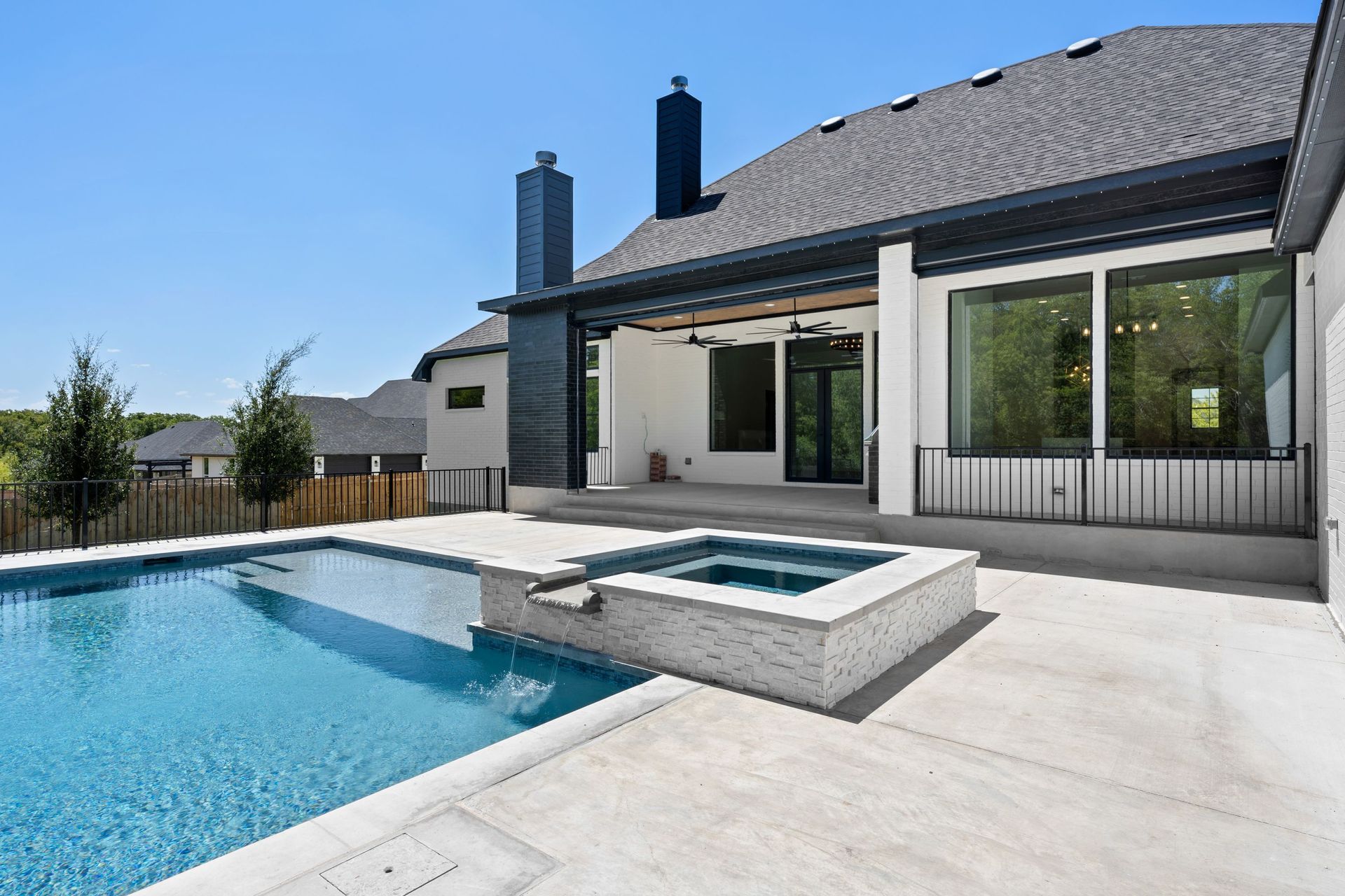Modern house patio with a swimming pool and hot tub under a blue sky