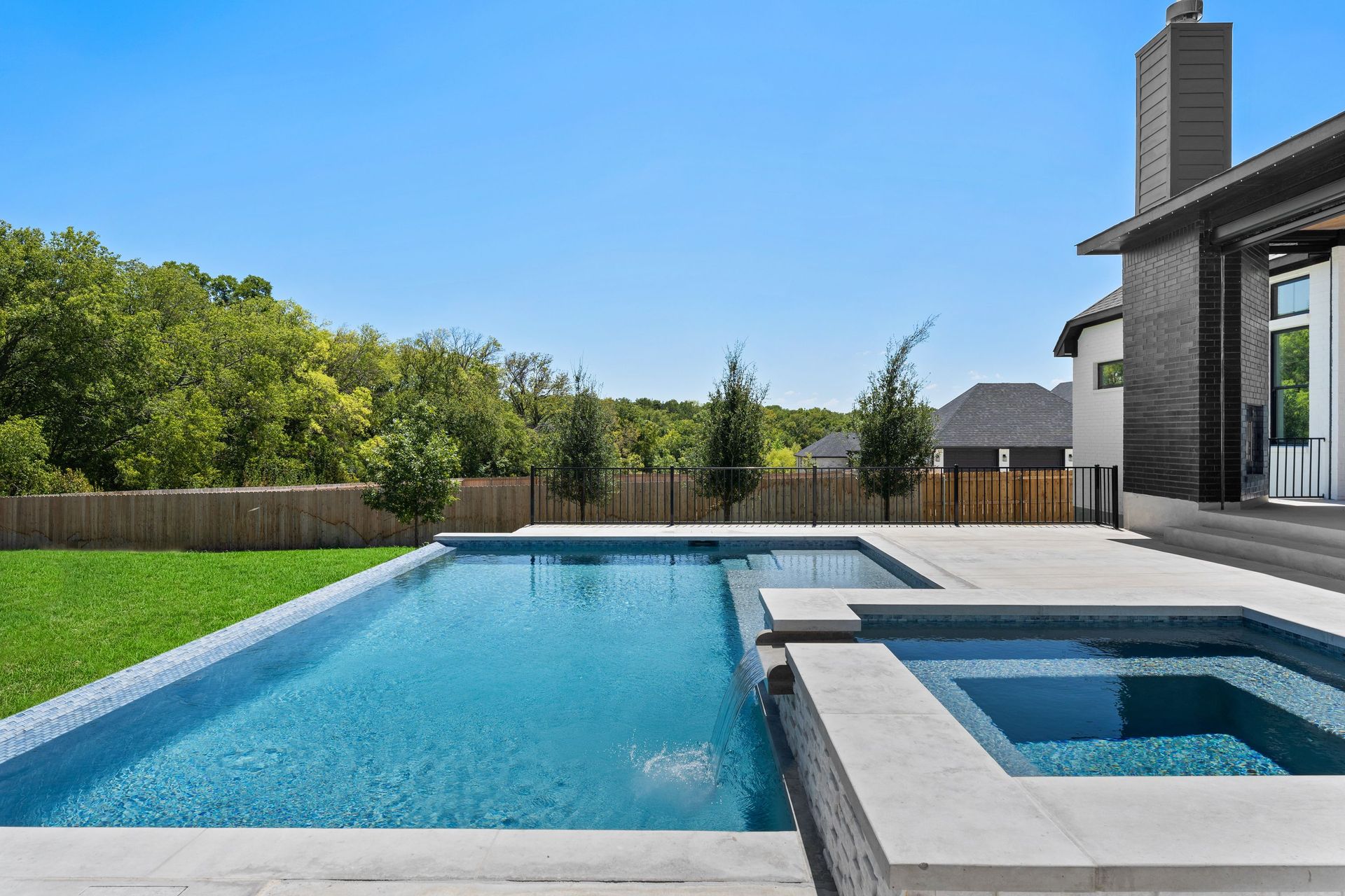 Modern backyard with a blue swimming pool, raised hot tub, and patio beside a house
