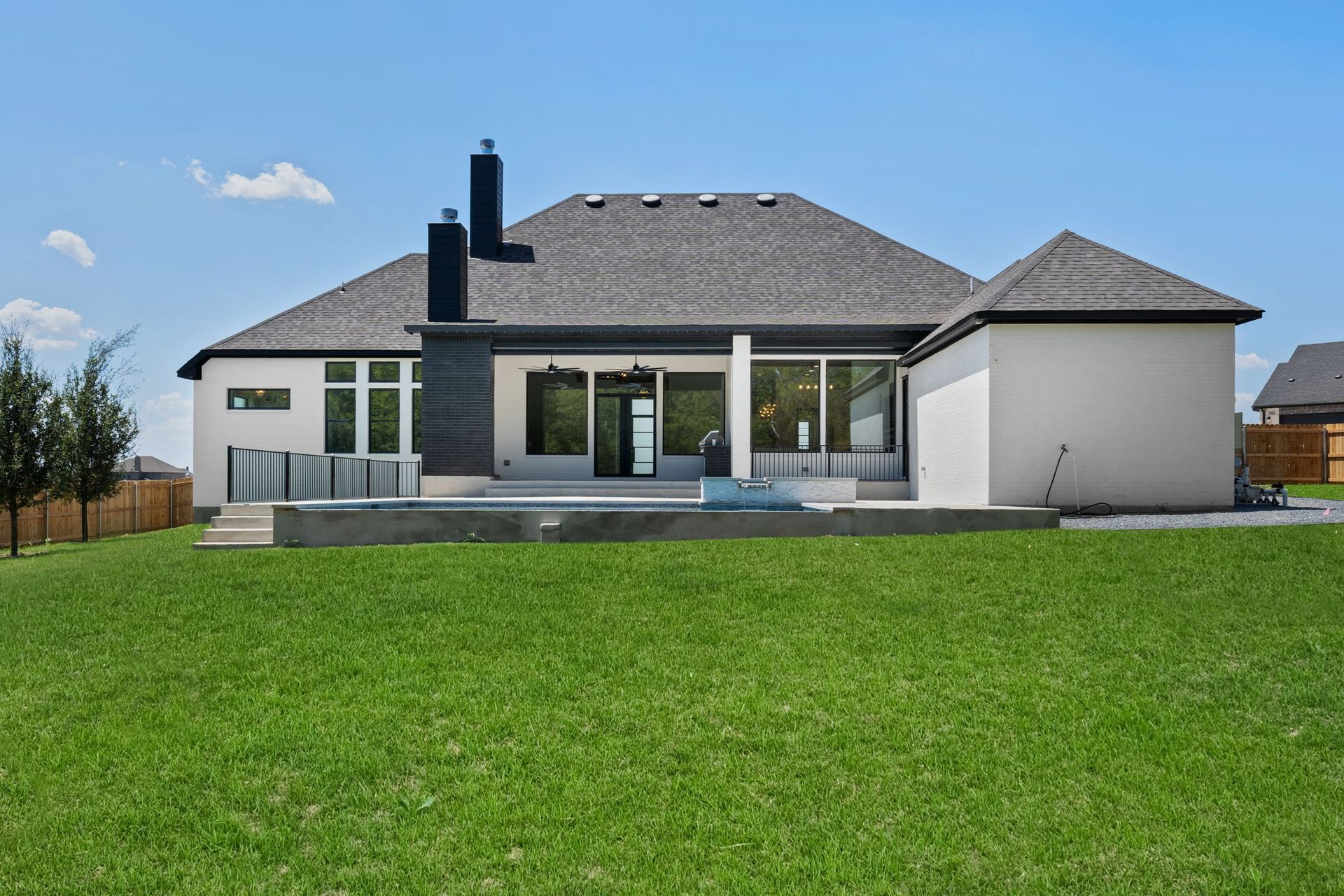 Modern single-story house with a gray roof, patio, and large green lawn under a blue sky
