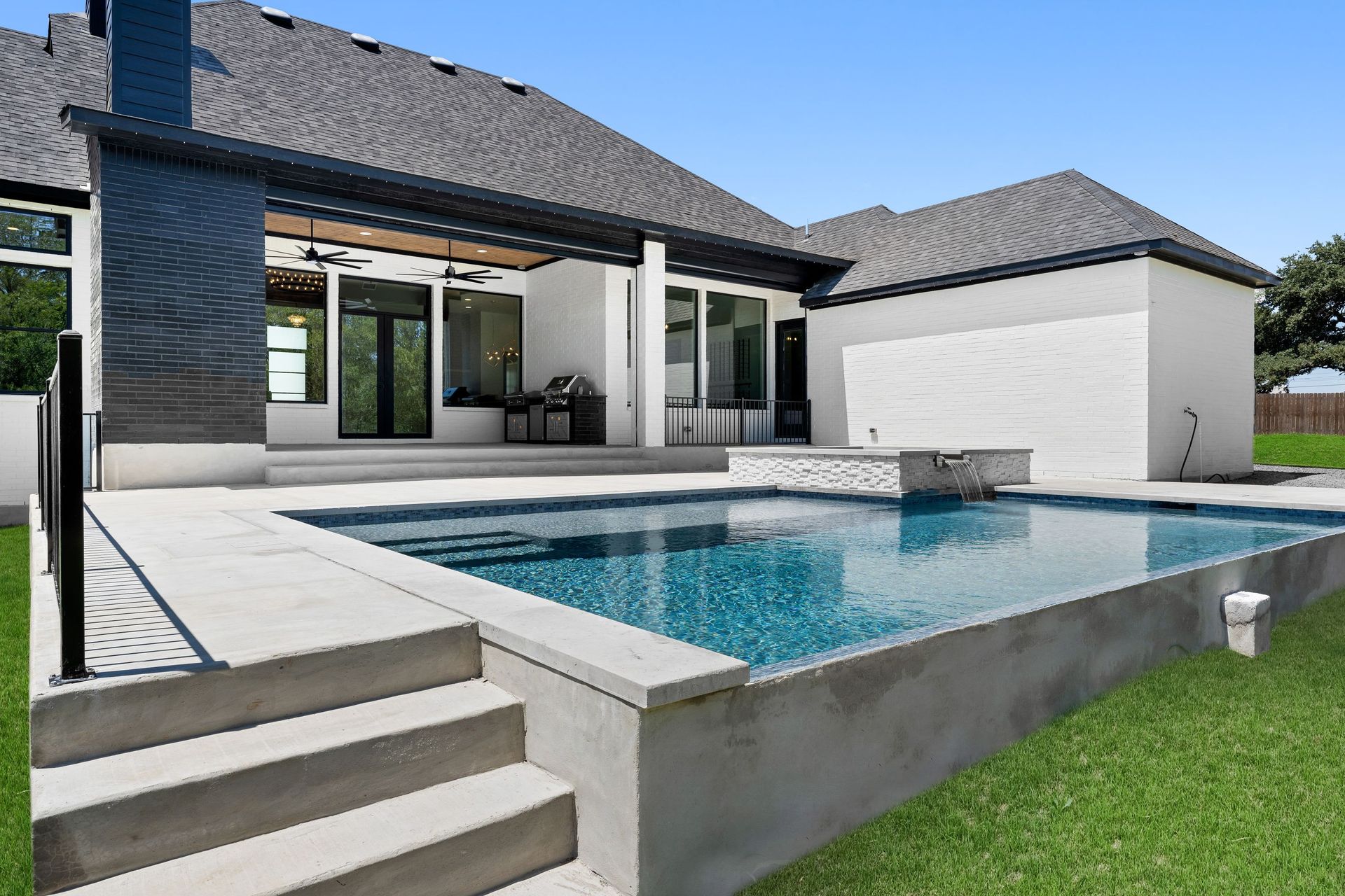 Modern house with a backyard pool, patio steps, and a green lawn