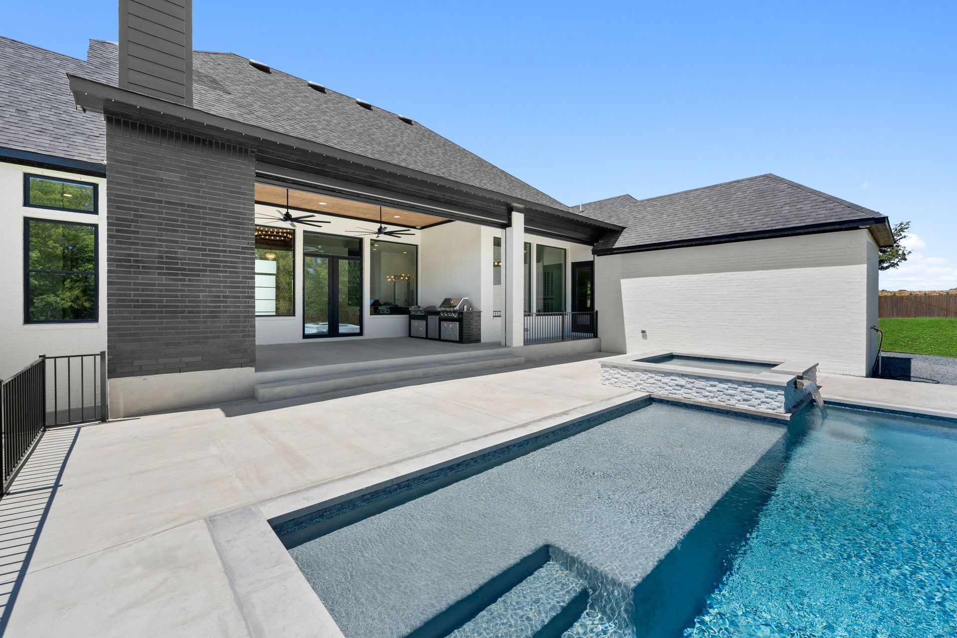 Modern patio with a swimming pool beside a contemporary house, featuring gray stone and white exterior walls