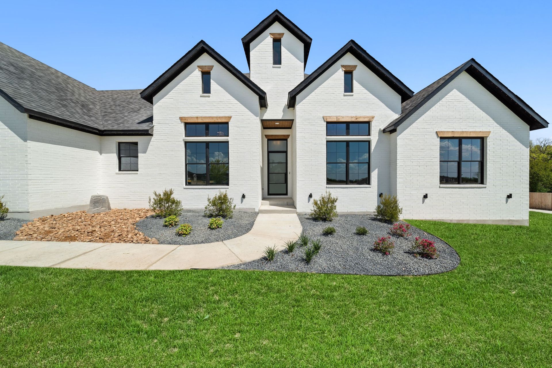 Modern white house with black trim, landscaped front yard, and green lawn under a blue sky