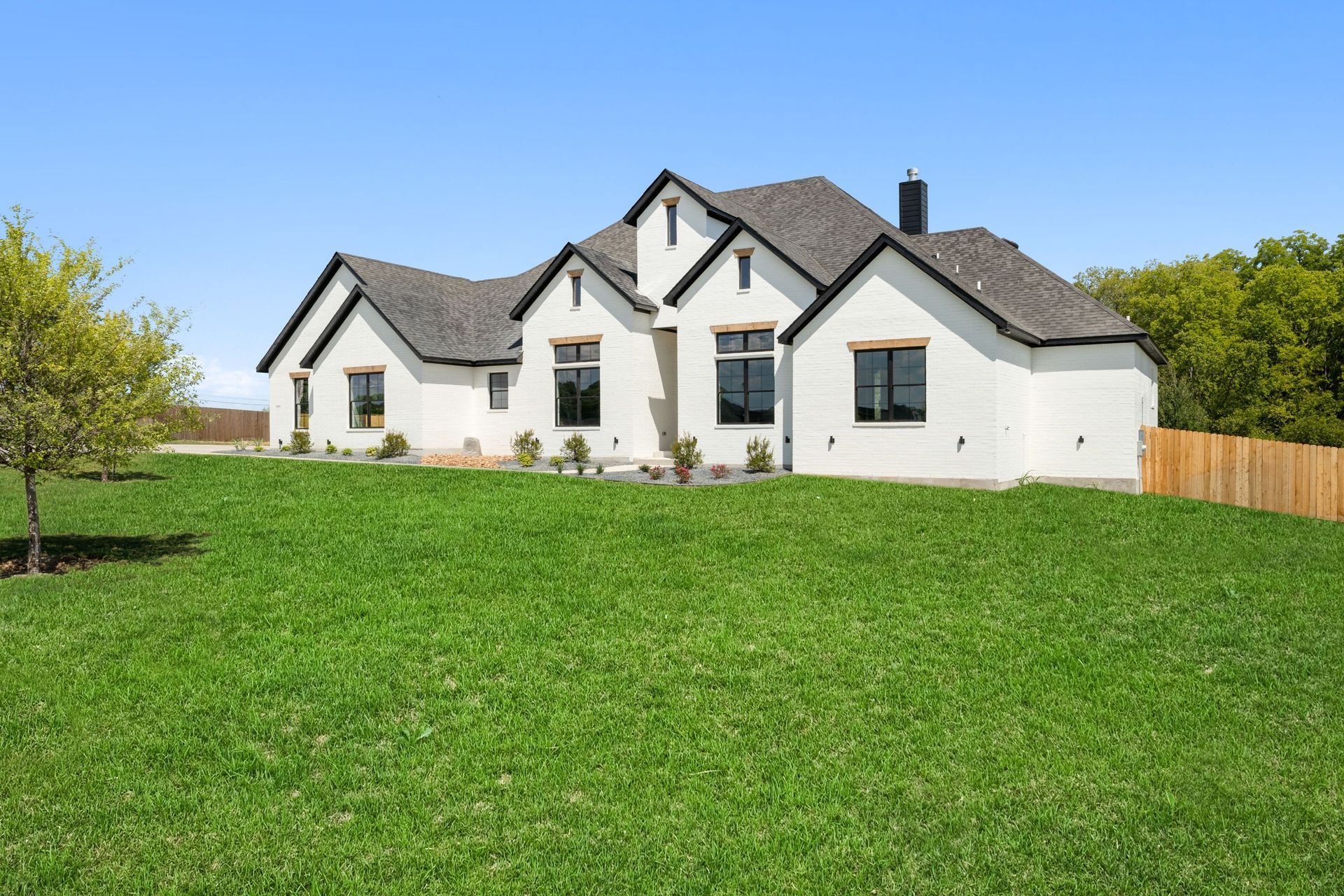 White house with black roof on a large green lawn under a clear blue sky