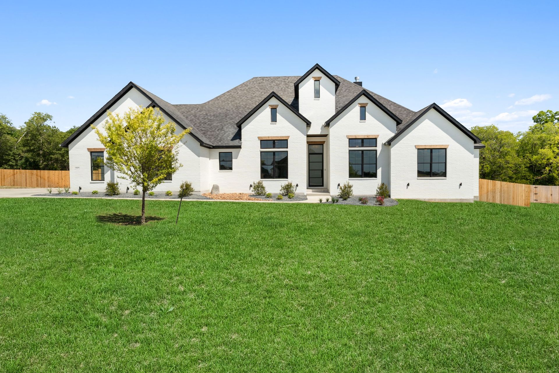 Large white suburban house with dark roof and green lawn under a clear blue sky