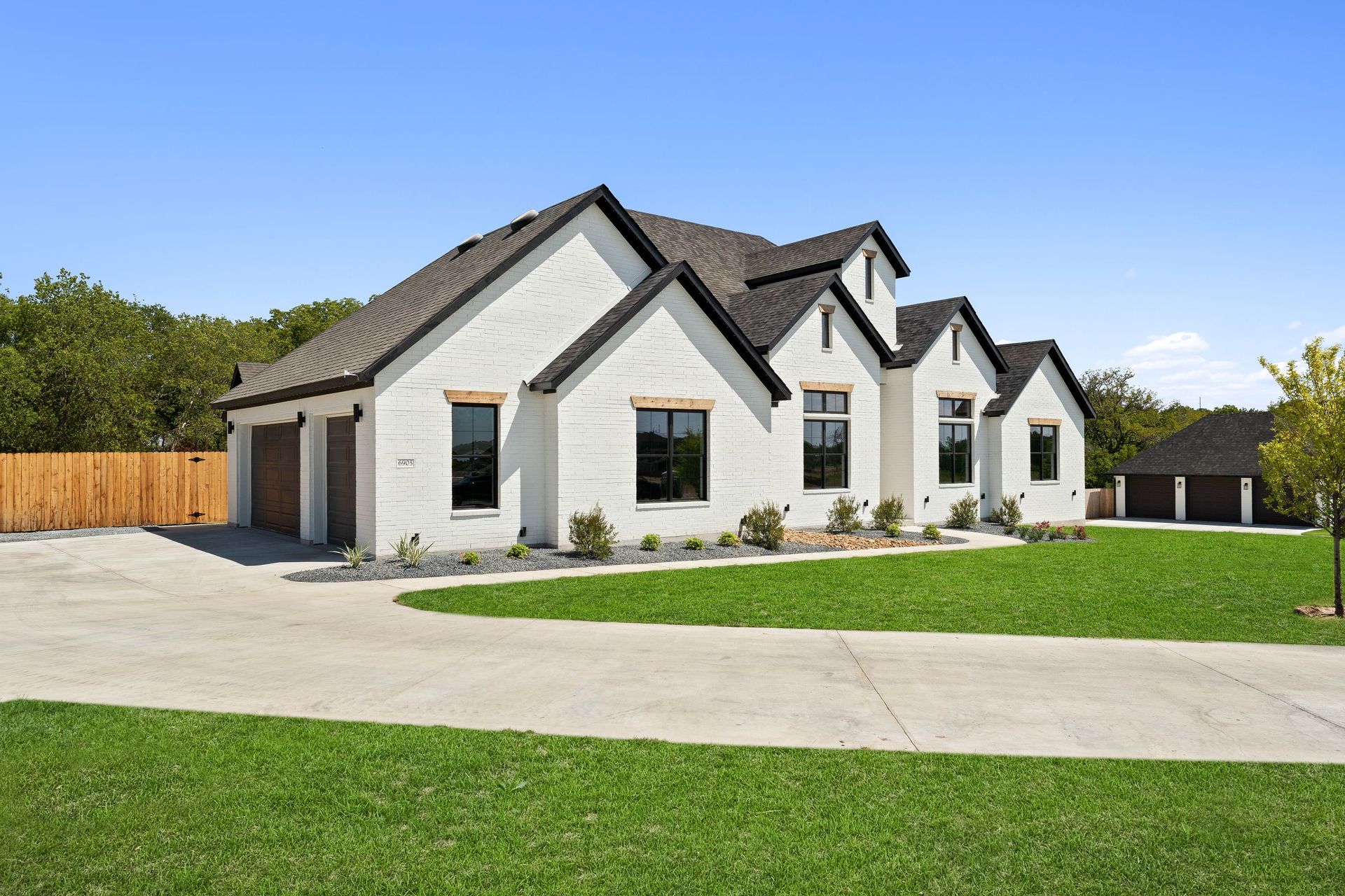 Modern white suburban house with gabled roofs, large driveway, and green lawn under a clear sky