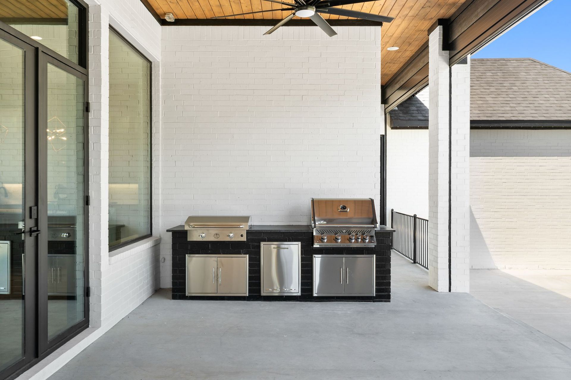 Covered patio with built-in outdoor grill and storage cabinets beside a house exterior