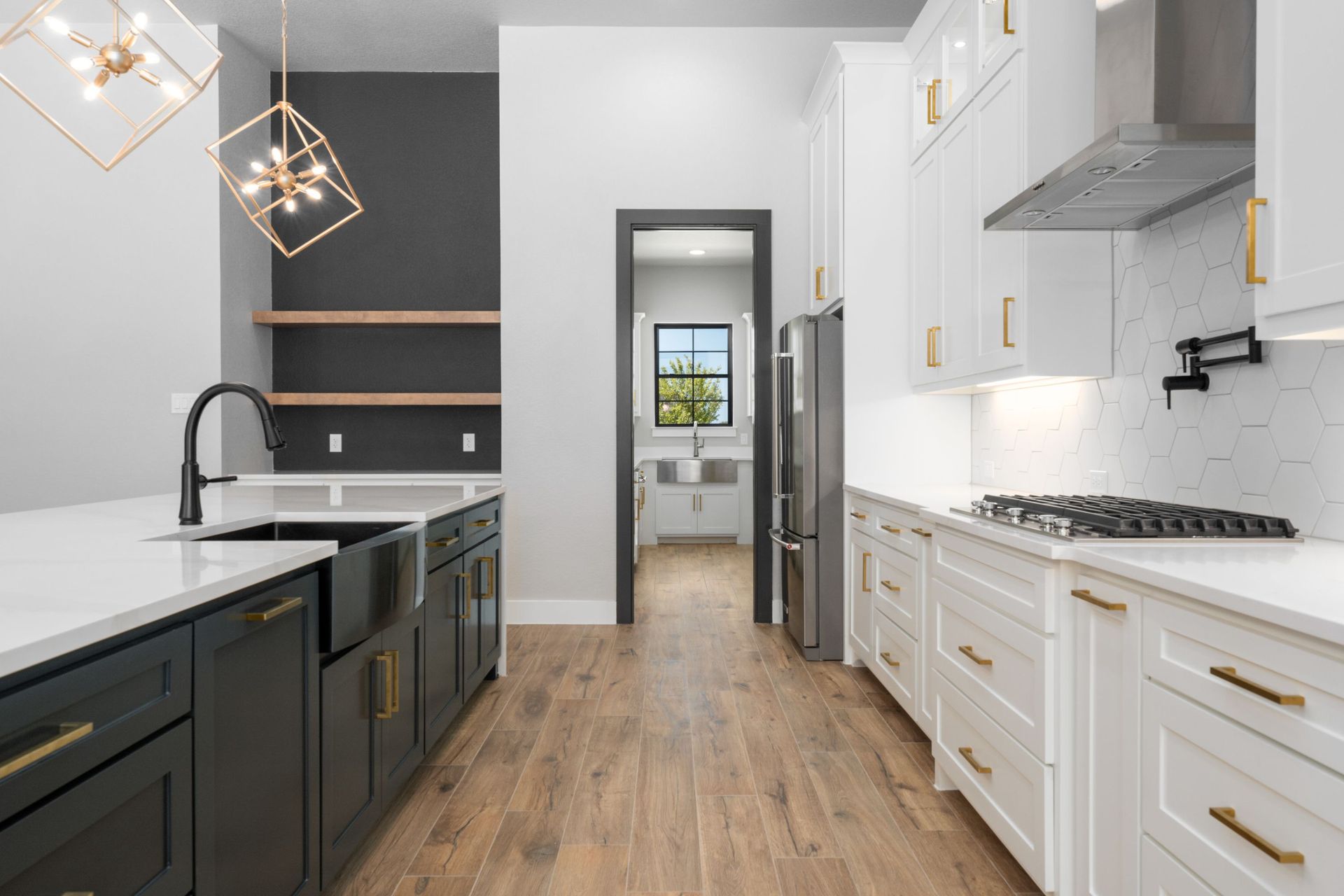 Modern kitchen with black and white cabinetry, wood floors, and a view into a hallway