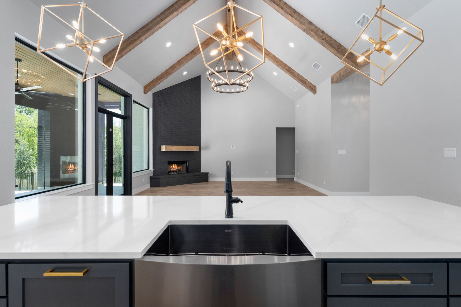 Modern open-concept kitchen with white counters, black island sink, and gold geometric chandeliers