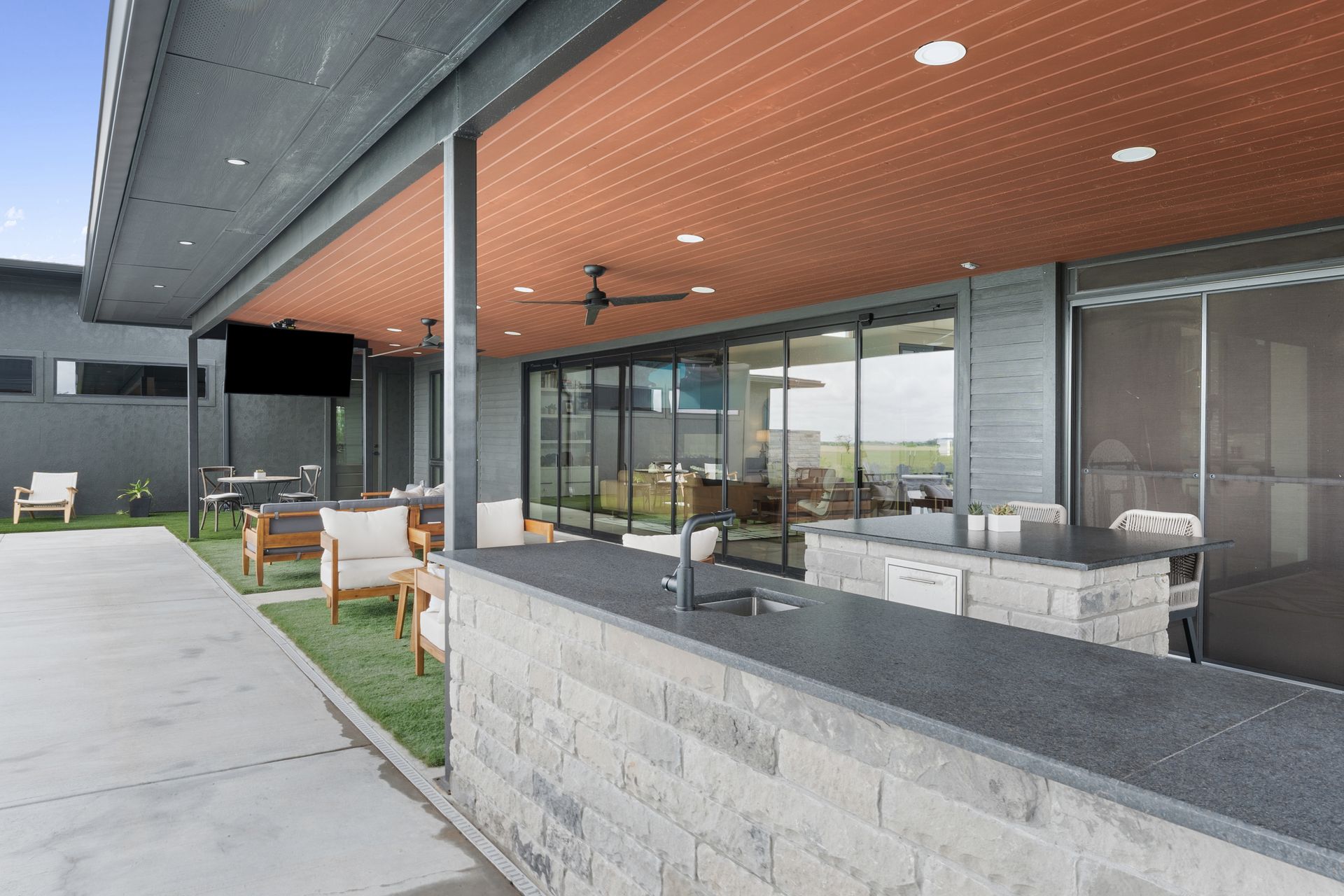 Modern covered patio with stone seating, ceiling fans, and glass walls overlooking a yard