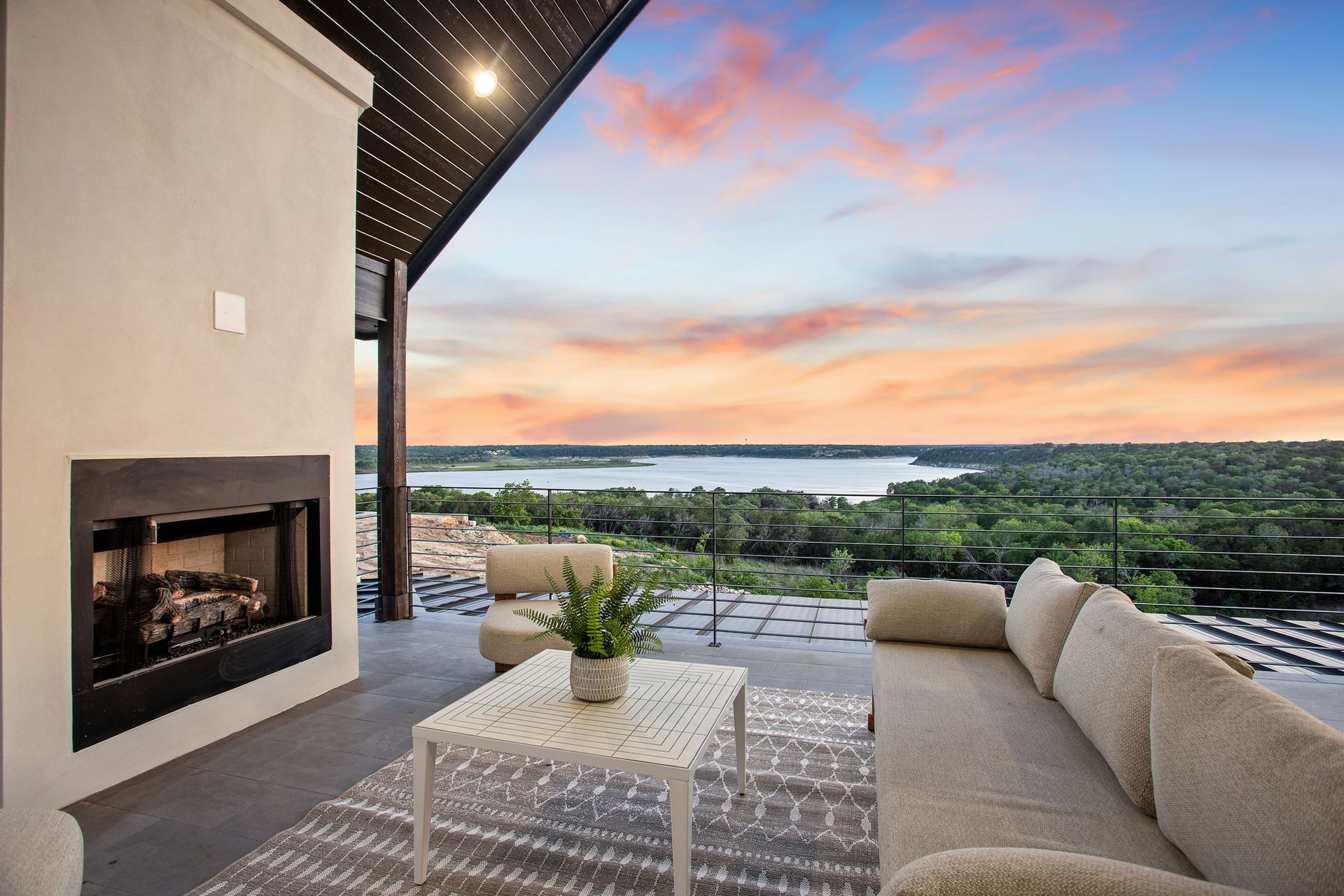 Modern patio with fireplace, wicker seating, and a sunset view over water.