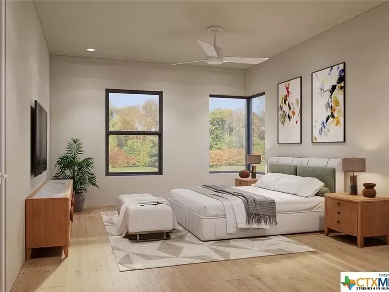 Bright bedroom with a bed, wooden nightstands, pouf, potted plant, and two windows with wall art.