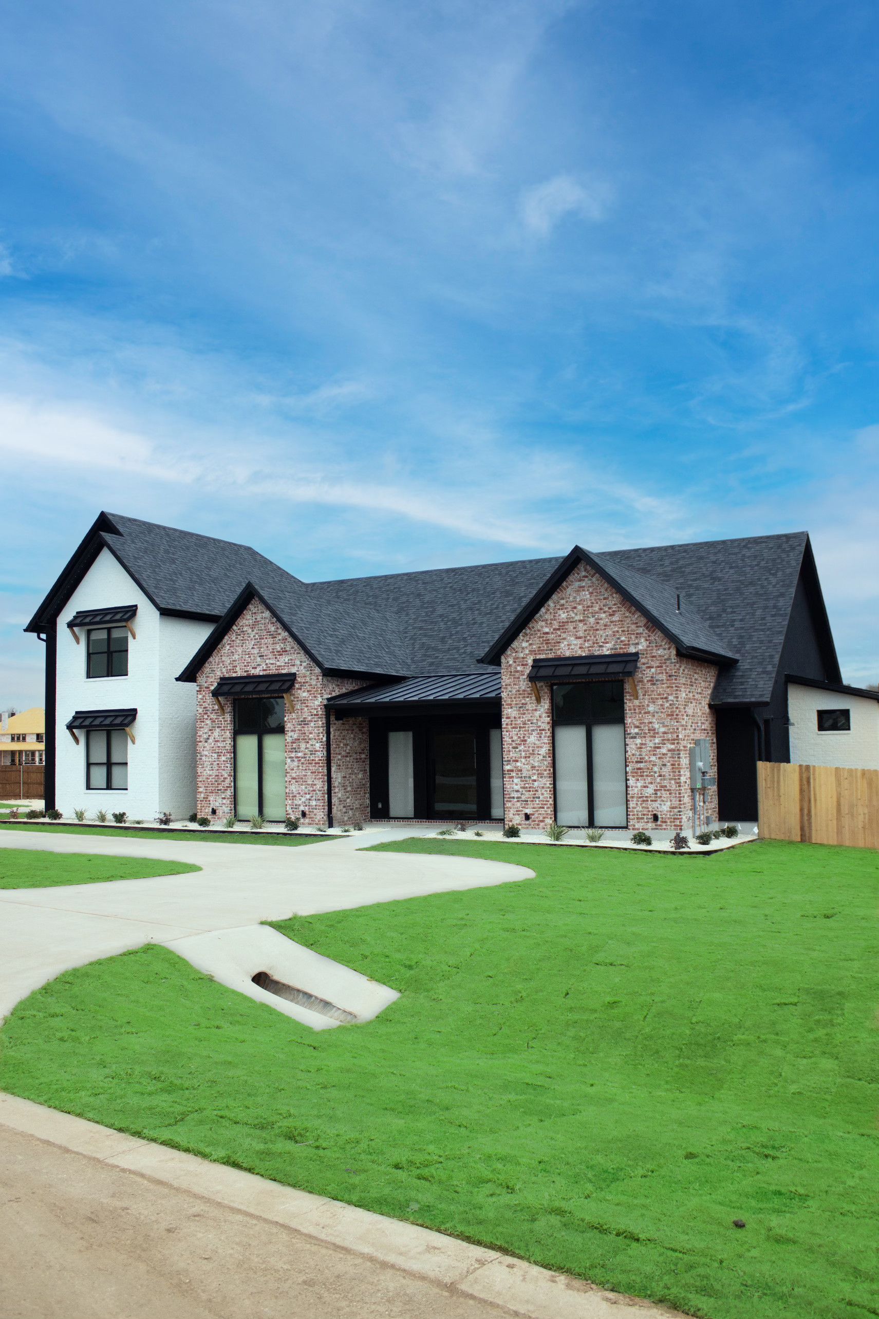 Modern brick-and-stone suburban house with a gray roof, green lawn, and blue sky