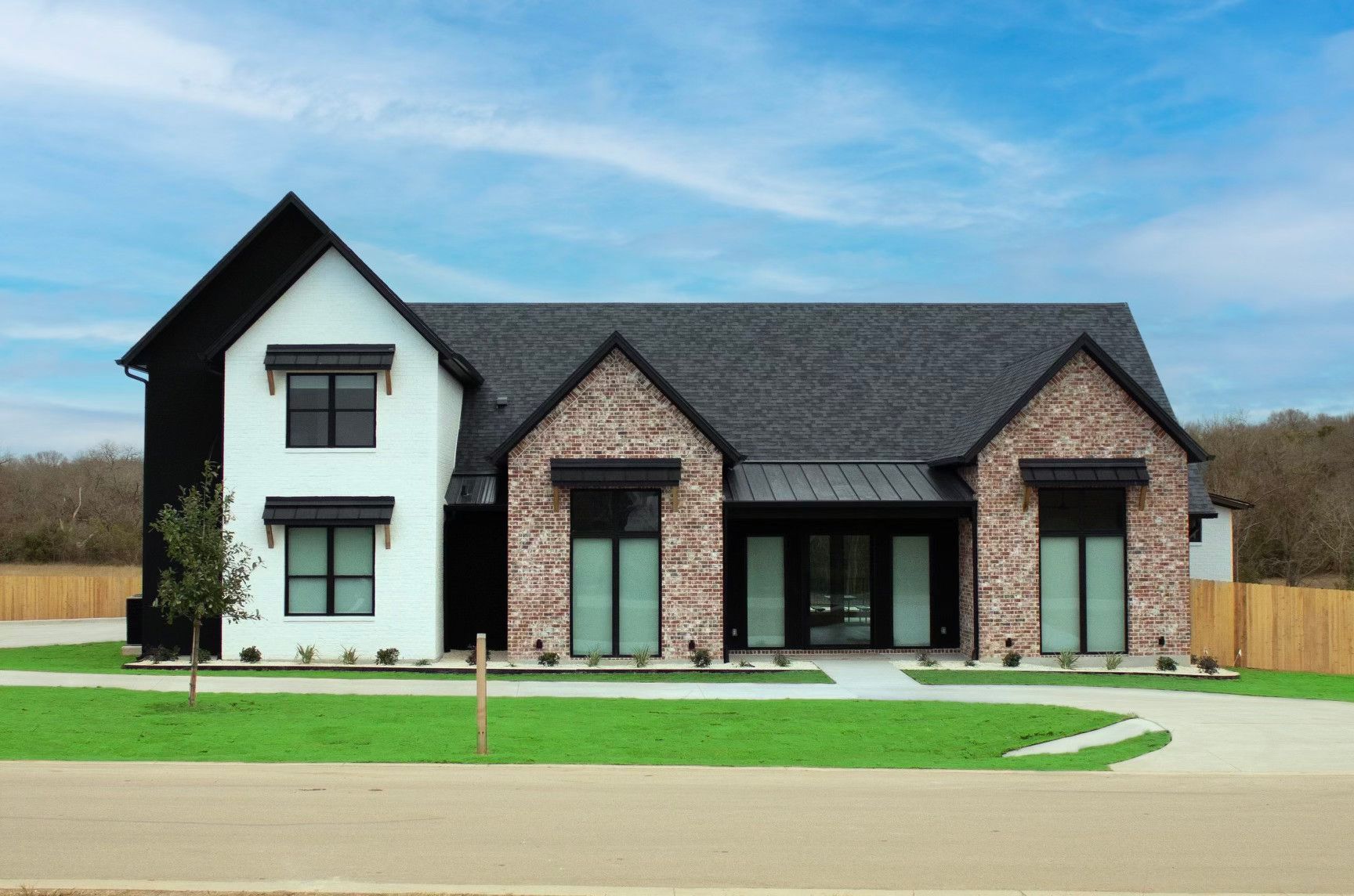Modern two-story house with white siding, brick facade, and green lawn under a blue sky