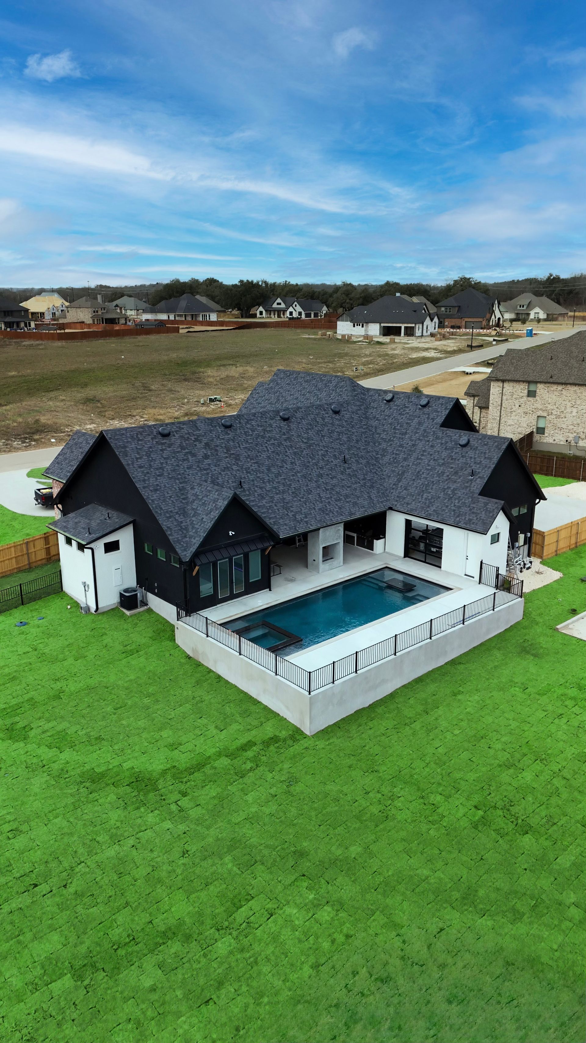 Modern black-roofed house with a pool and bright green lawn in a suburban area