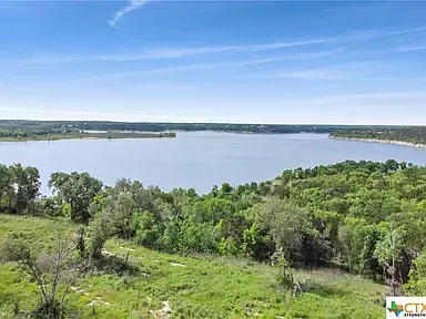 Wide lake with calm water, green shoreline, and blue sky with wispy clouds