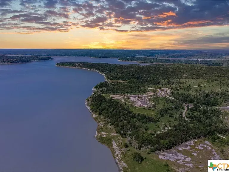 Aerial view of a forested riverbank at sunset with a wide blue river and colorful clouds.