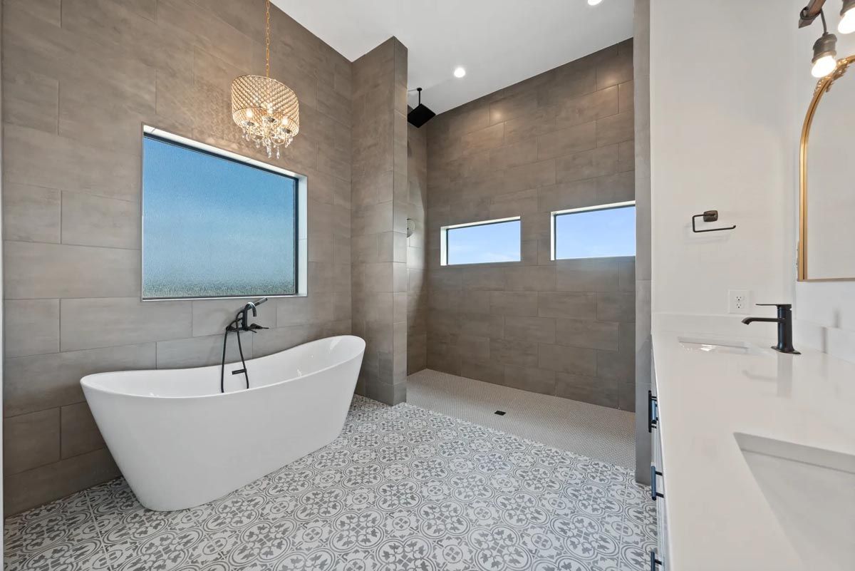 Modern bathroom with freestanding tub, large window, and gray tile walls and floor