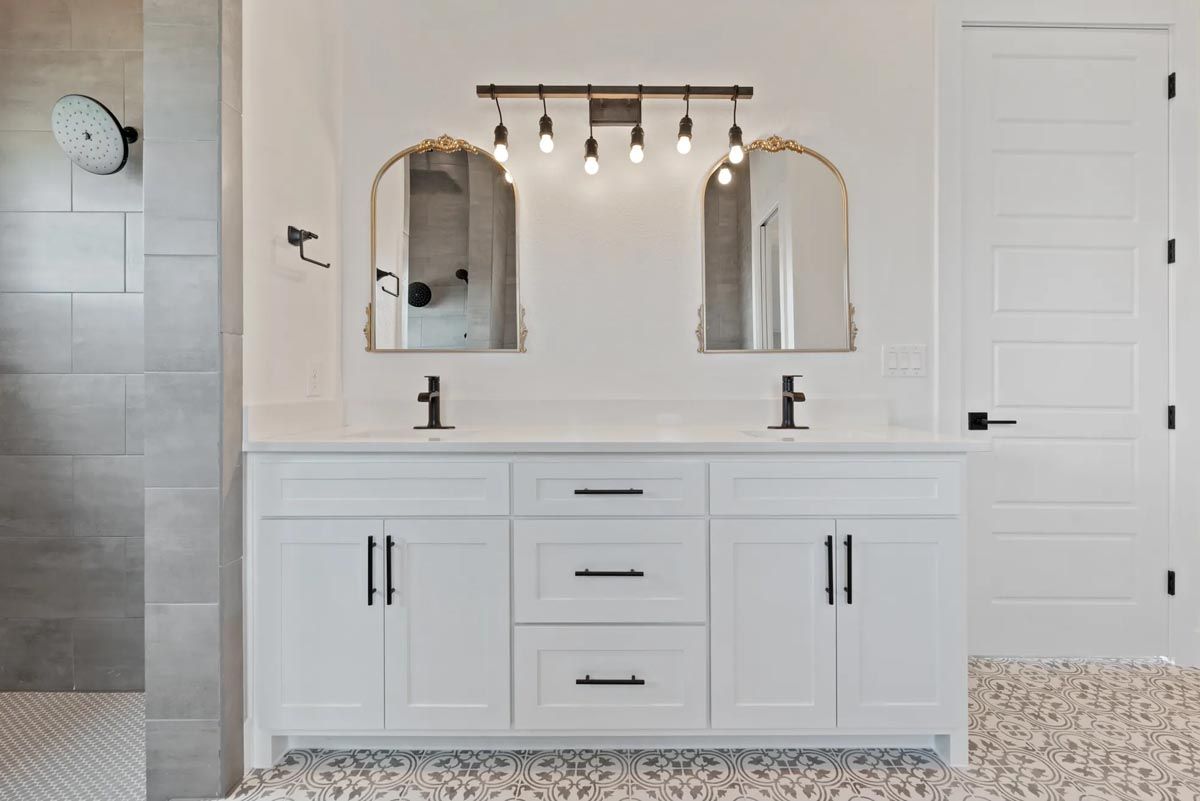Modern white bathroom vanity with double mirrors, black fixtures, and pebble flooring