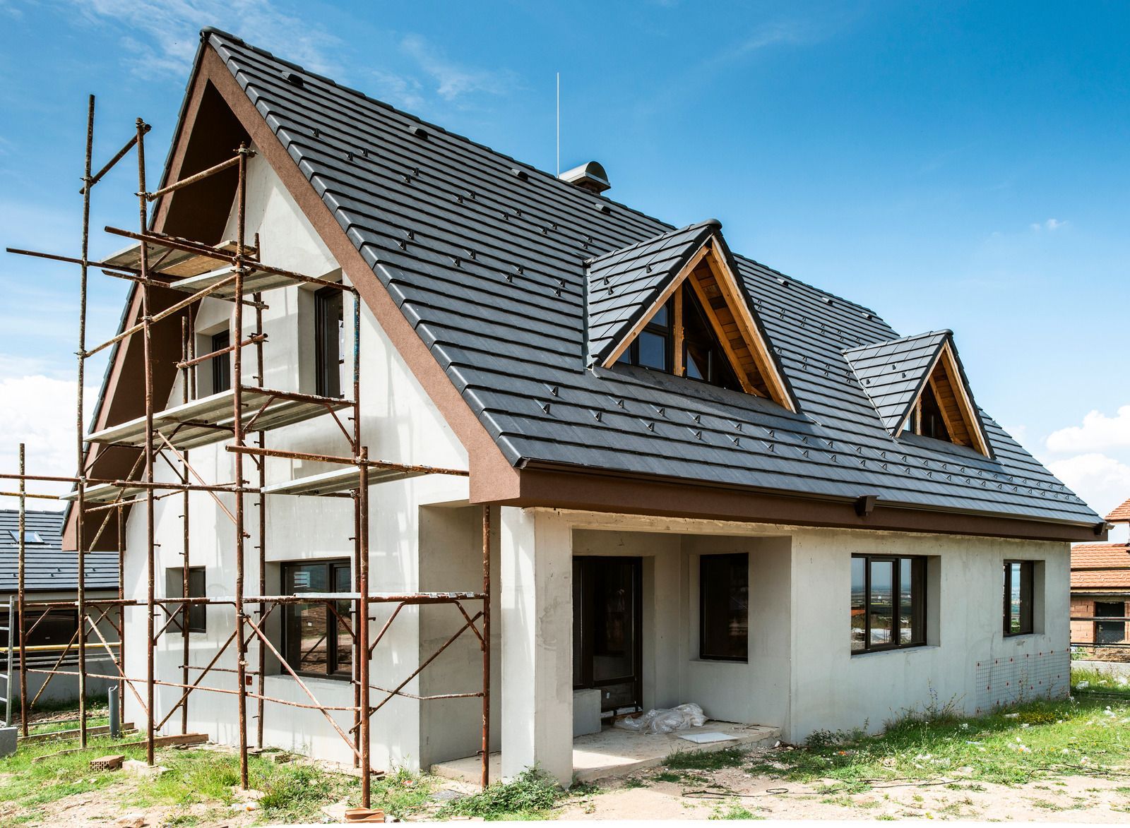 House under construction with scaffolding and a dark gray roof under a clear blue sky