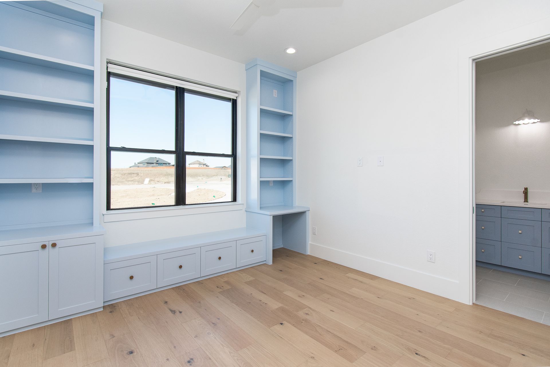Bright room with blue built-in shelves, window seat, wood floor, and doorway to a bathroom