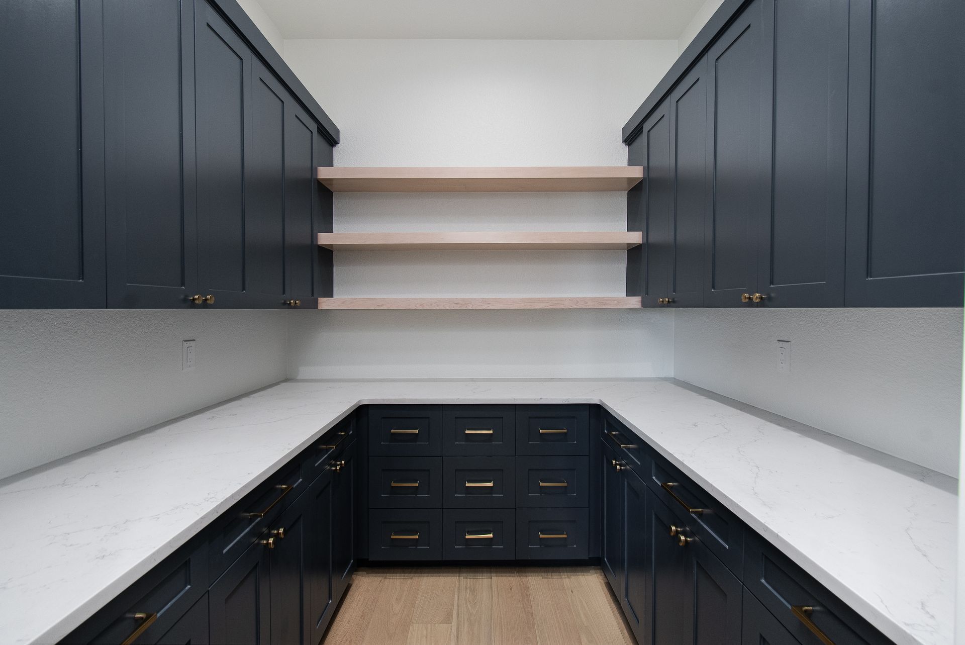 Modern U-shaped kitchen with dark navy cabinets, white countertops, and open wooden shelves.