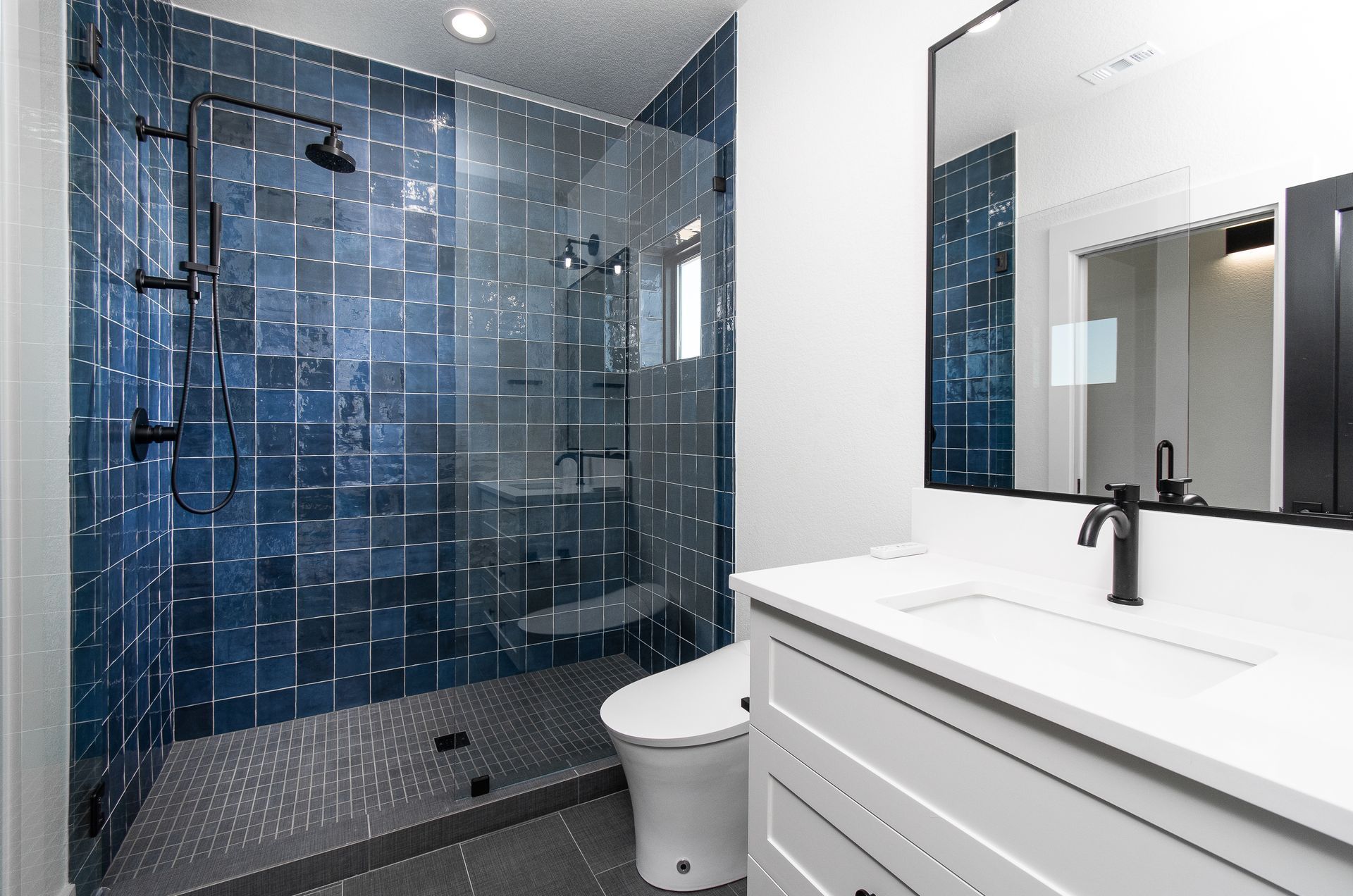 Modern bathroom with glass shower, dark tile, and white vanity with mirror
