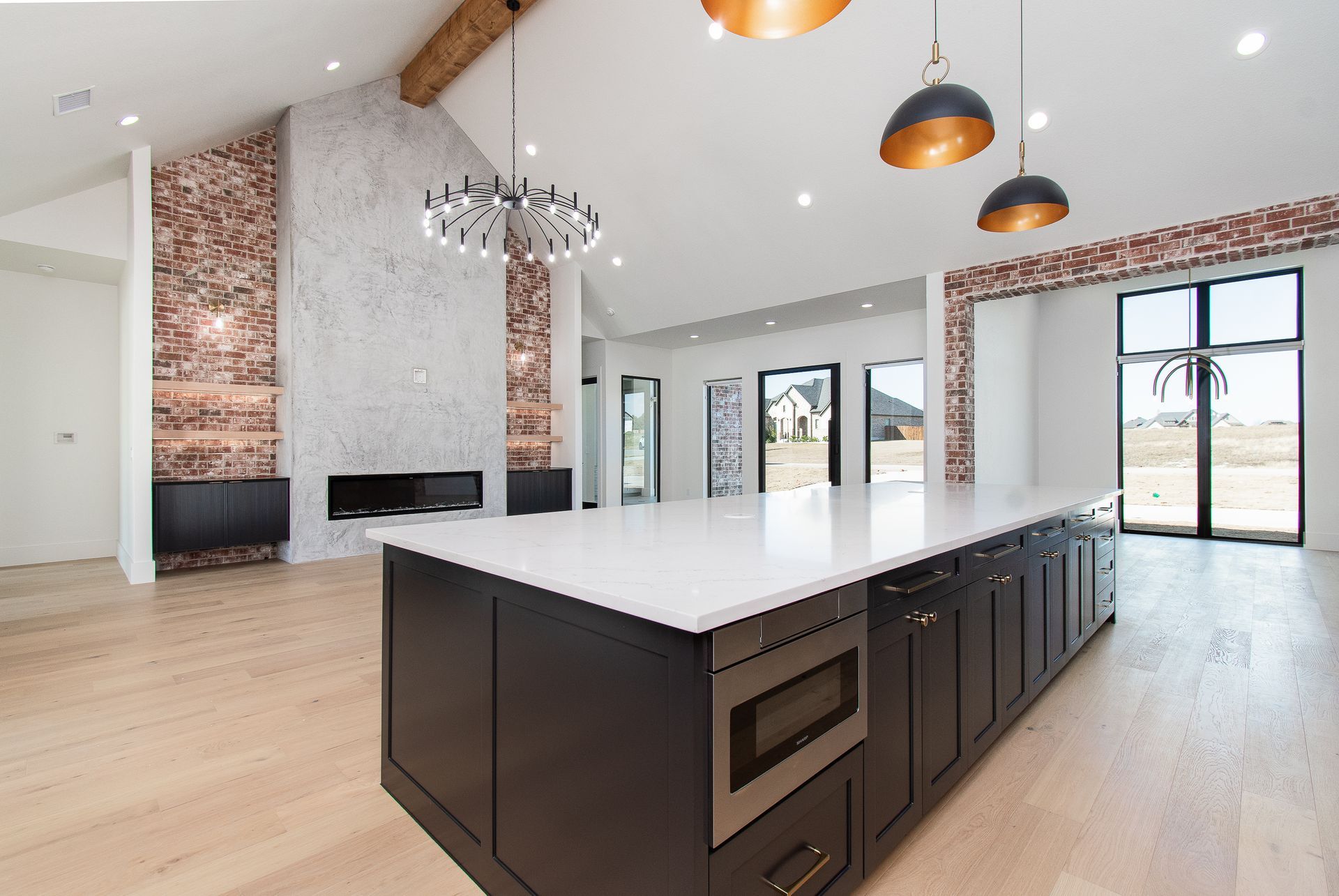 Spacious modern kitchen with dark island, white countertops, brick accents, and large windows