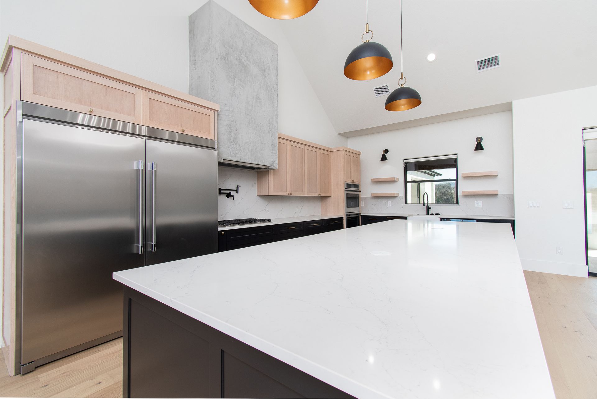 Modern white kitchen with stainless steel appliances, black island, and pendant lights
