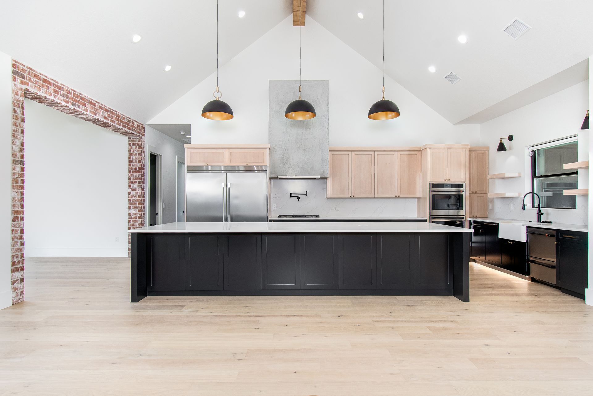 Modern kitchen with large black island, light wood cabinets, and pendant lights in an open, bright room