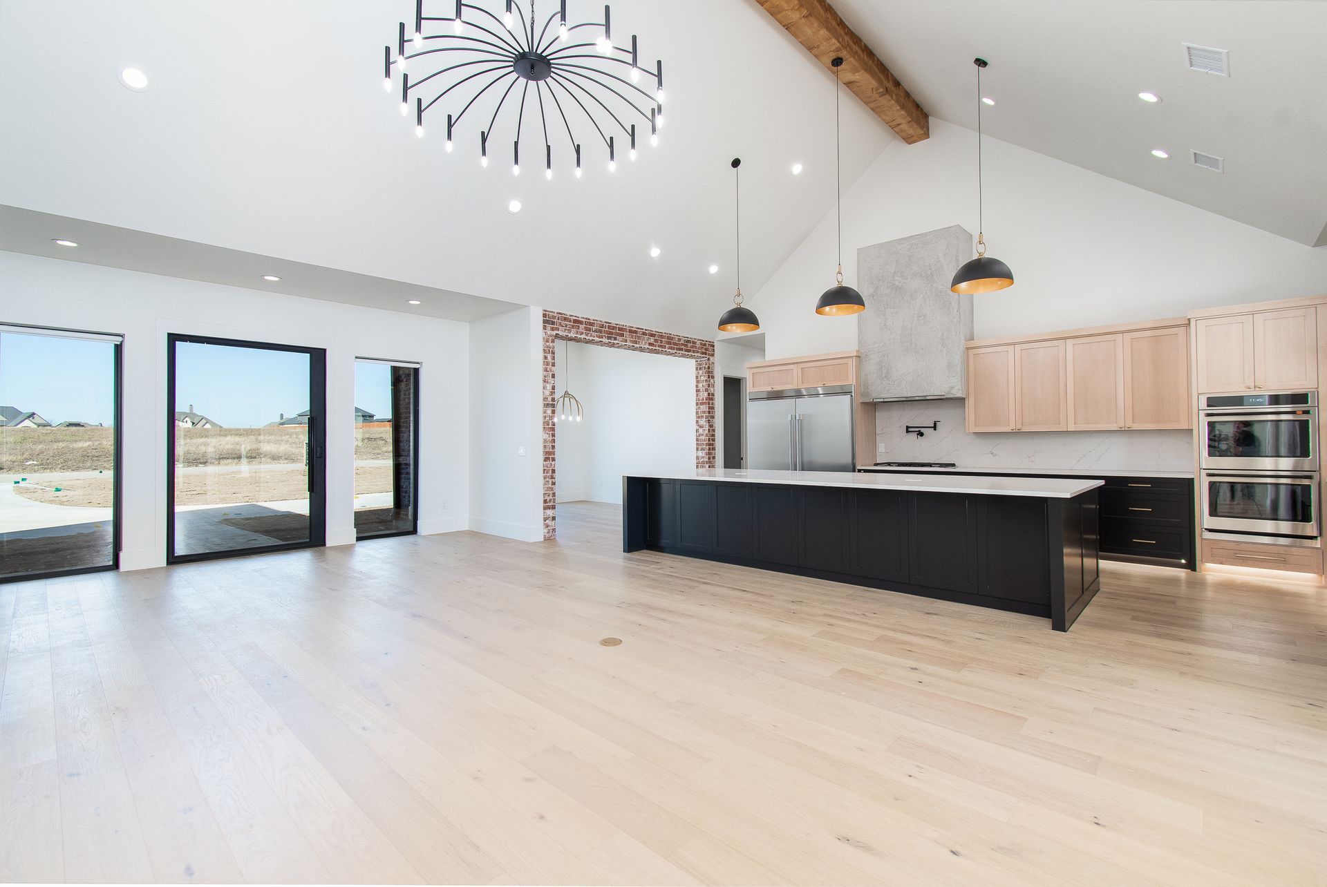 Bright modern kitchen with black island, light wood cabinets, high ceilings, and large windows overlooking a desert view