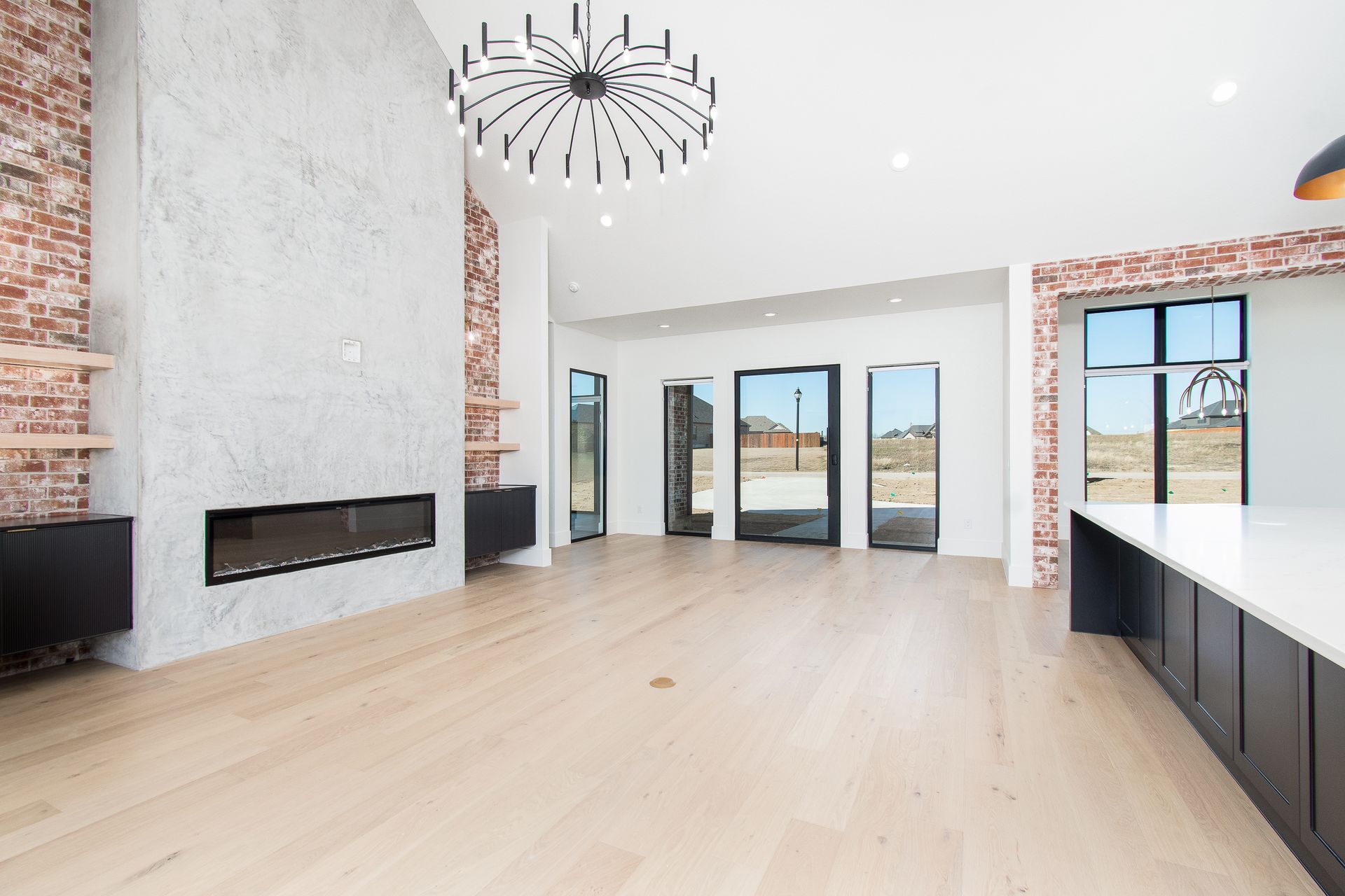 Modern empty living room with light wood floors, white walls, large windows, and a black chandelier