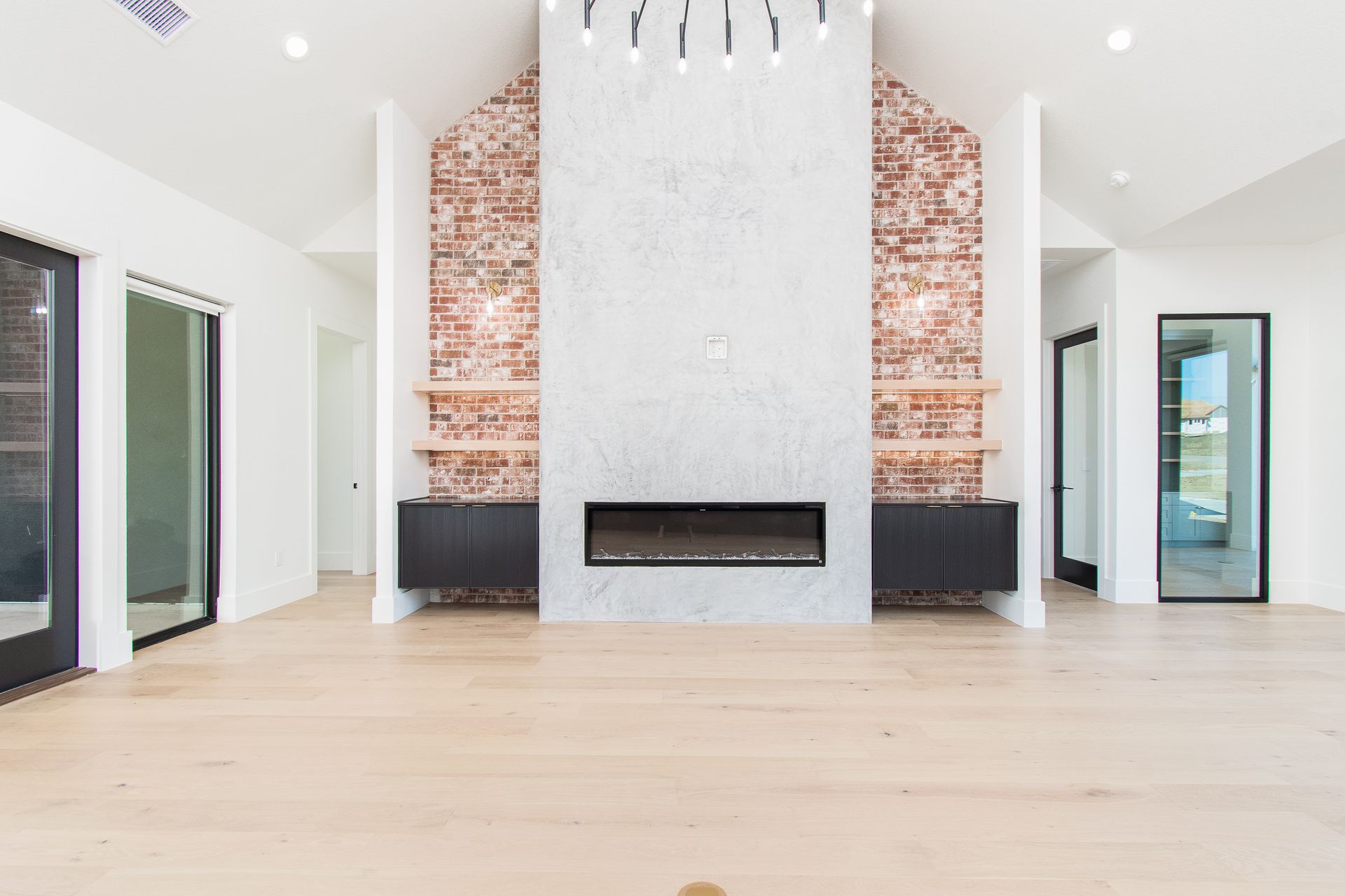 Bright modern living room with a white fireplace, exposed brick accent wall, and light wood floors