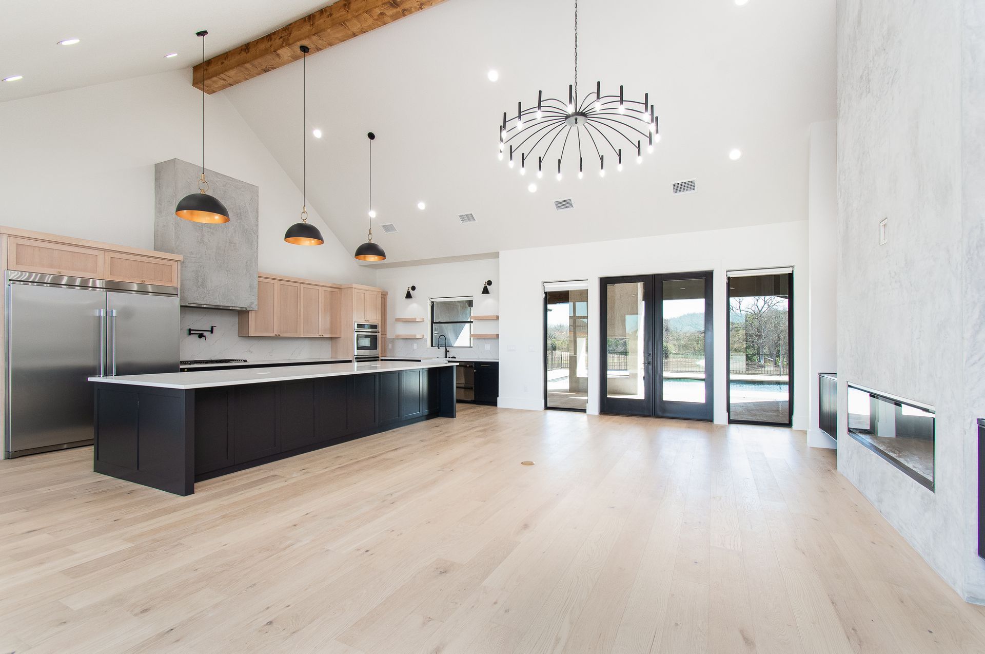 Bright modern kitchen and living space with black island, white walls, wood floors, and large glass doors