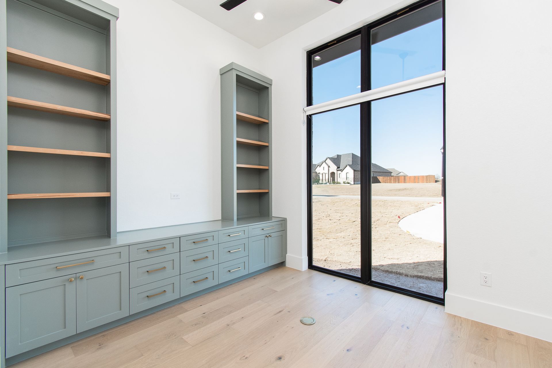 Built-in blue-gray cabinetry in a bright room with large black-framed windows and light wood floors