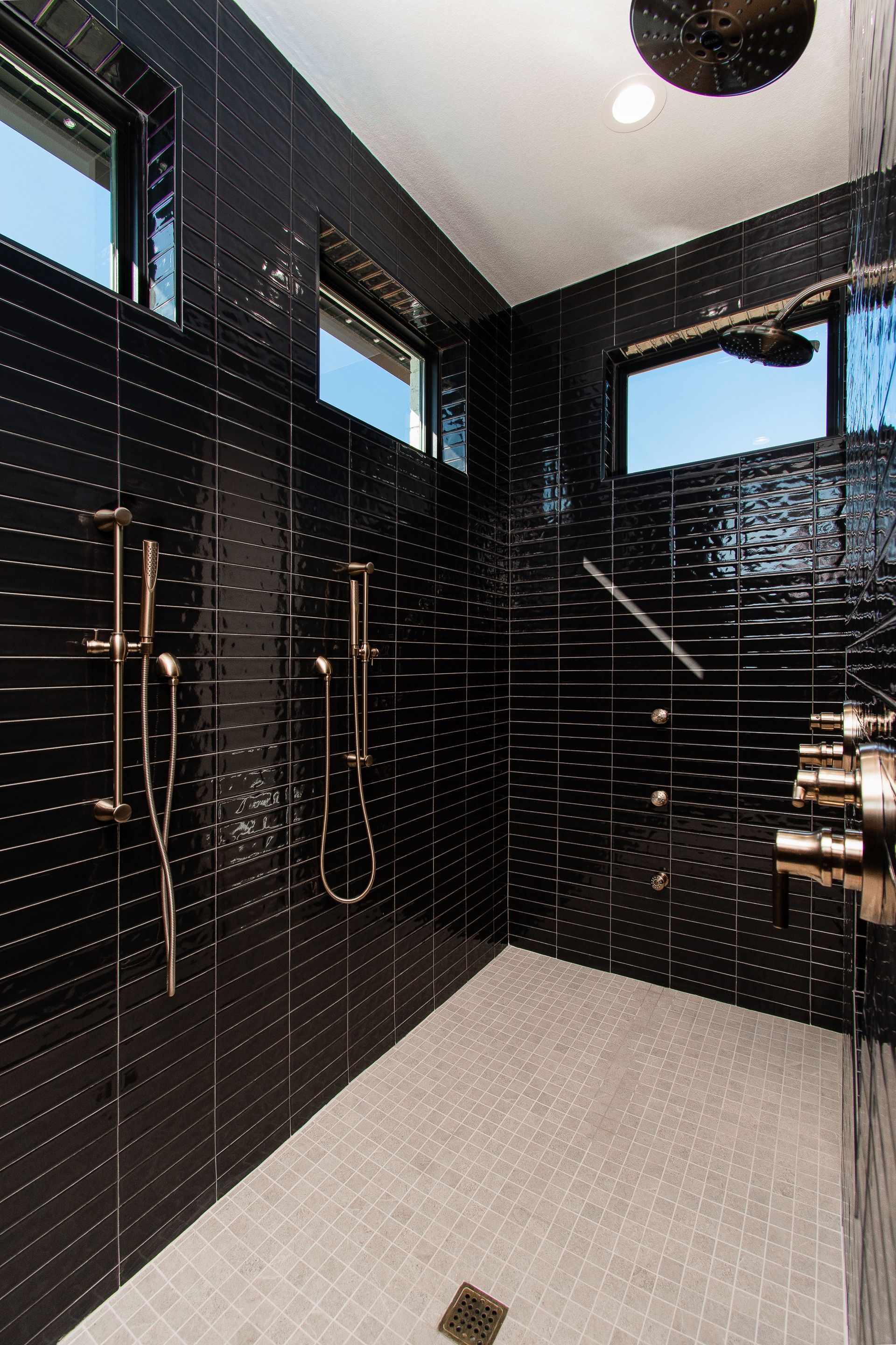 Modern black-tiled shower with multiple showerheads and a white tiled floor.