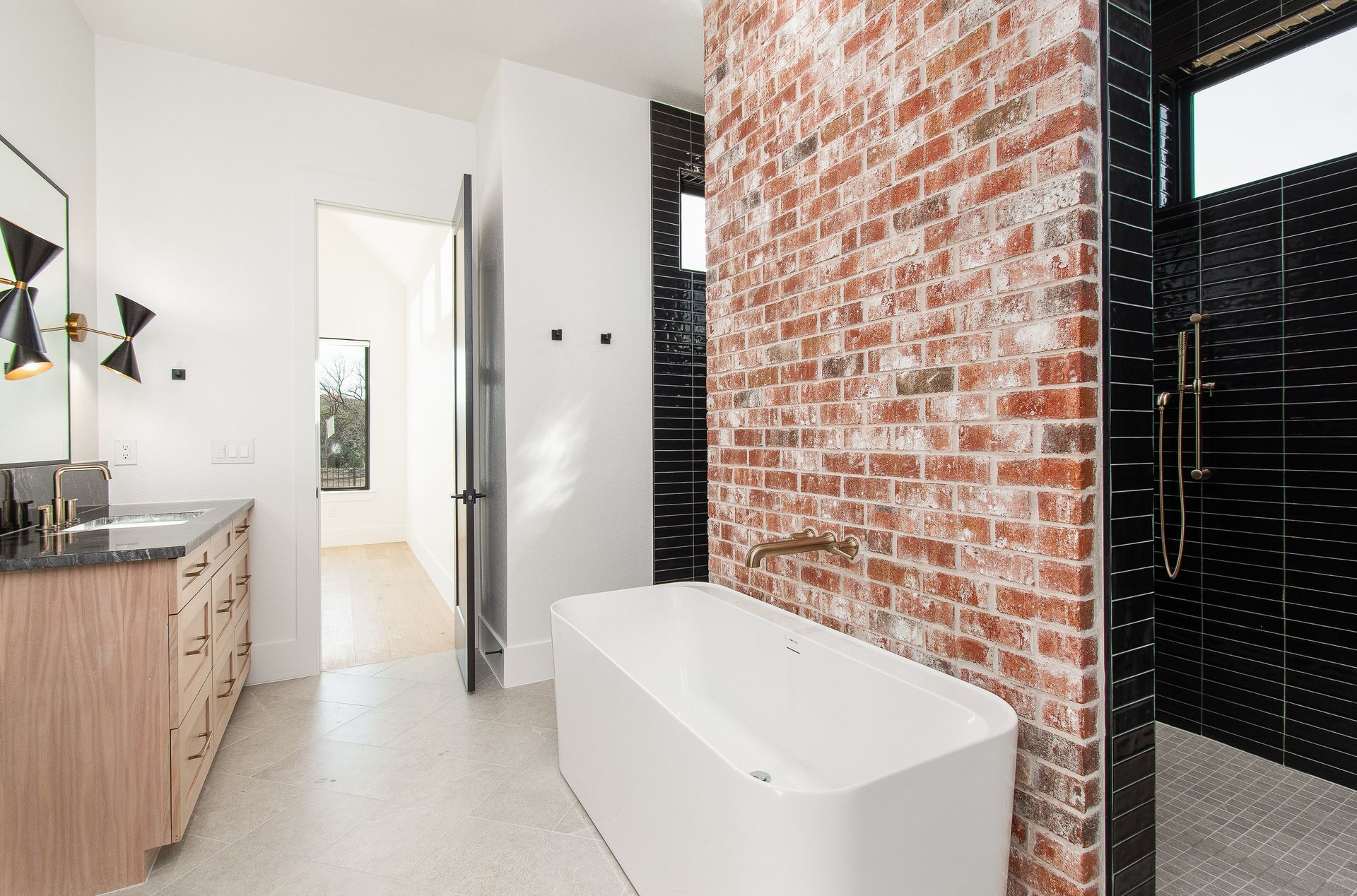 Modern bathroom with brick accent wall, black shower, wood vanity, and white freestanding tub