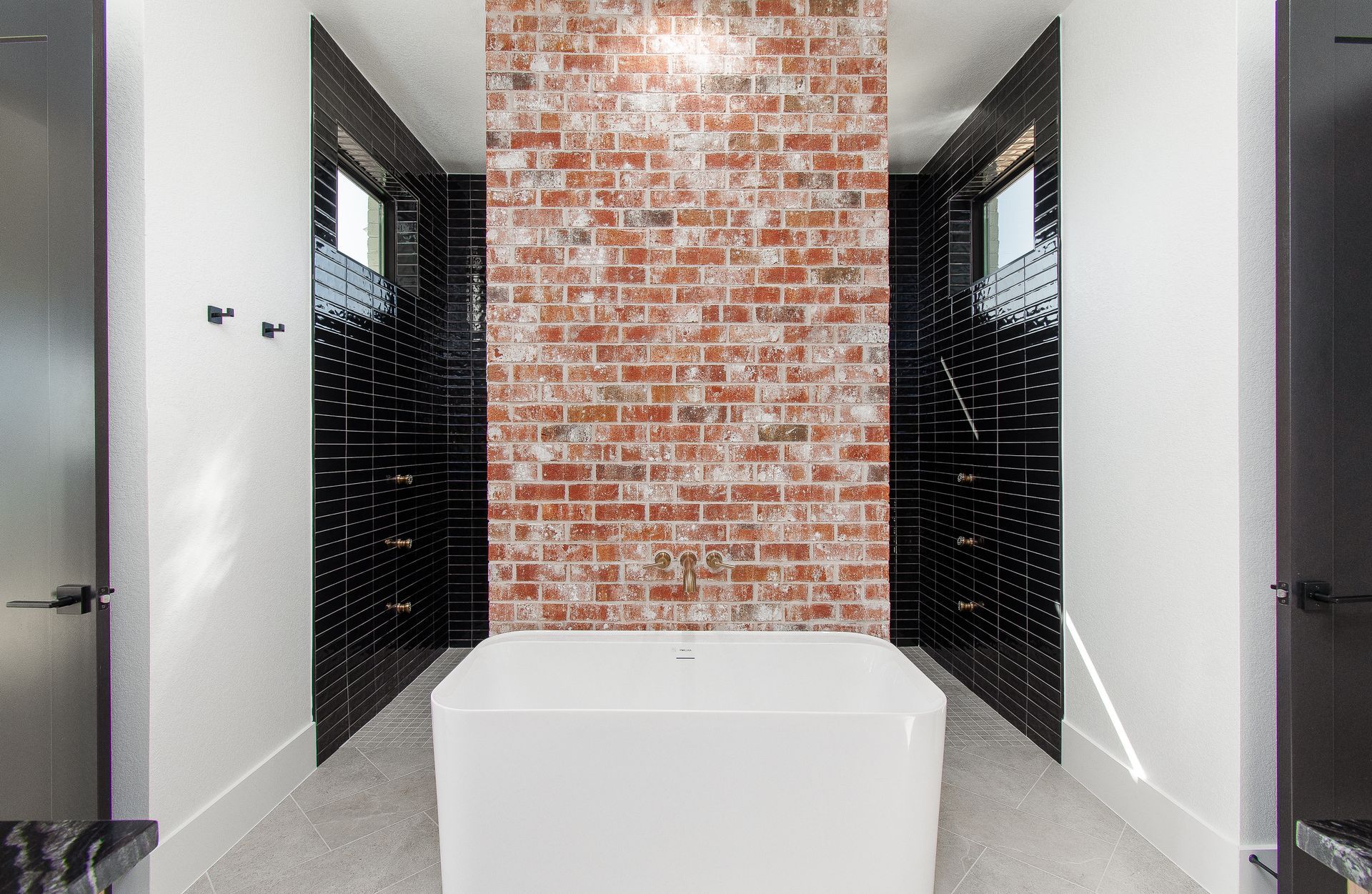 Modern bathroom with freestanding tub, brick accent wall, and black shower alcoves