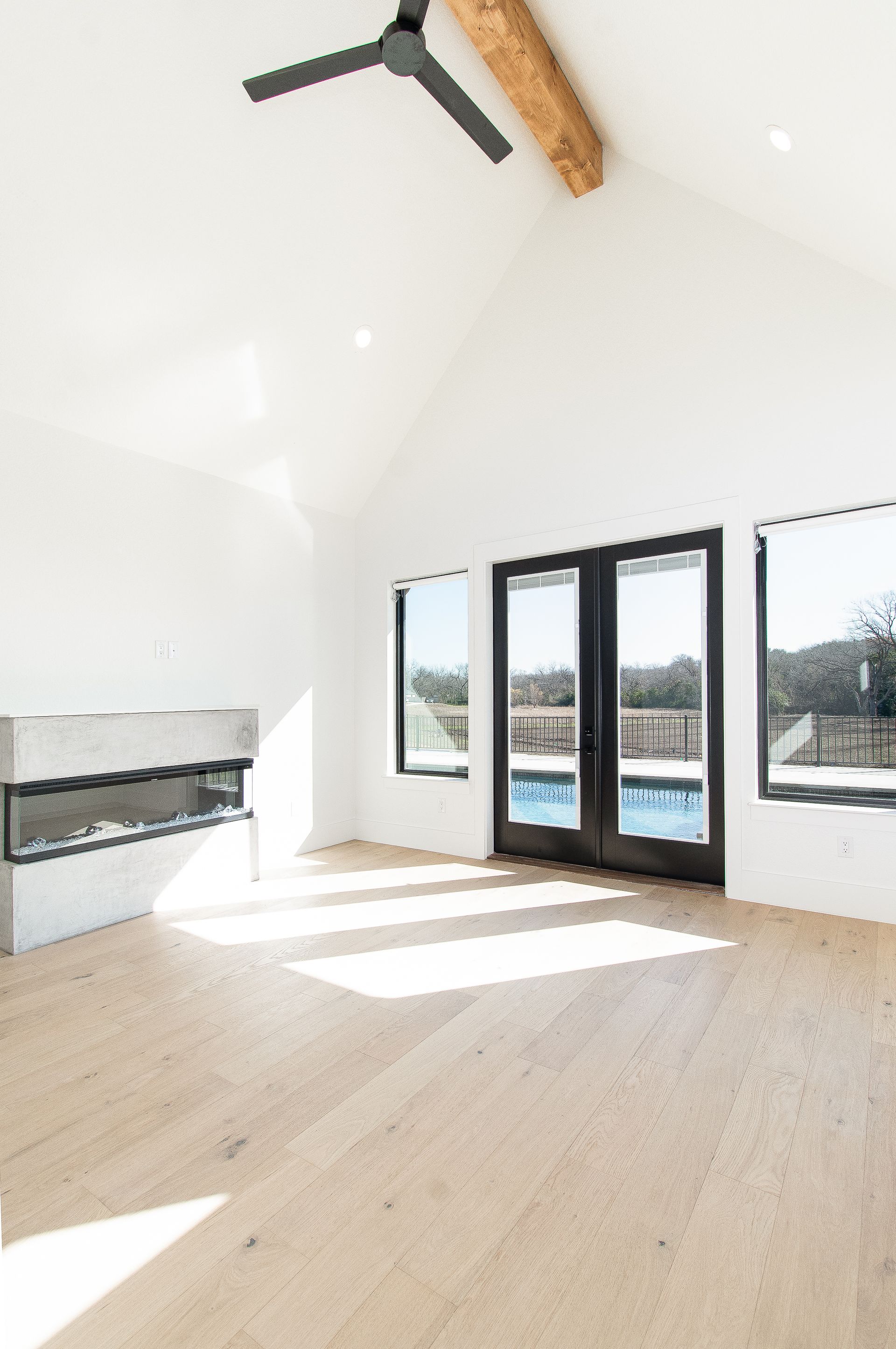 Bright empty living room with vaulted ceiling, black ceiling fan, fireplace, and glass doors opening to a balcony