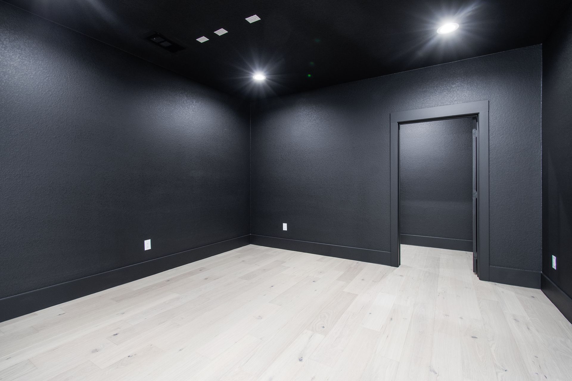 Empty modern room with black walls, white floor, recessed ceiling lights, and an open doorway