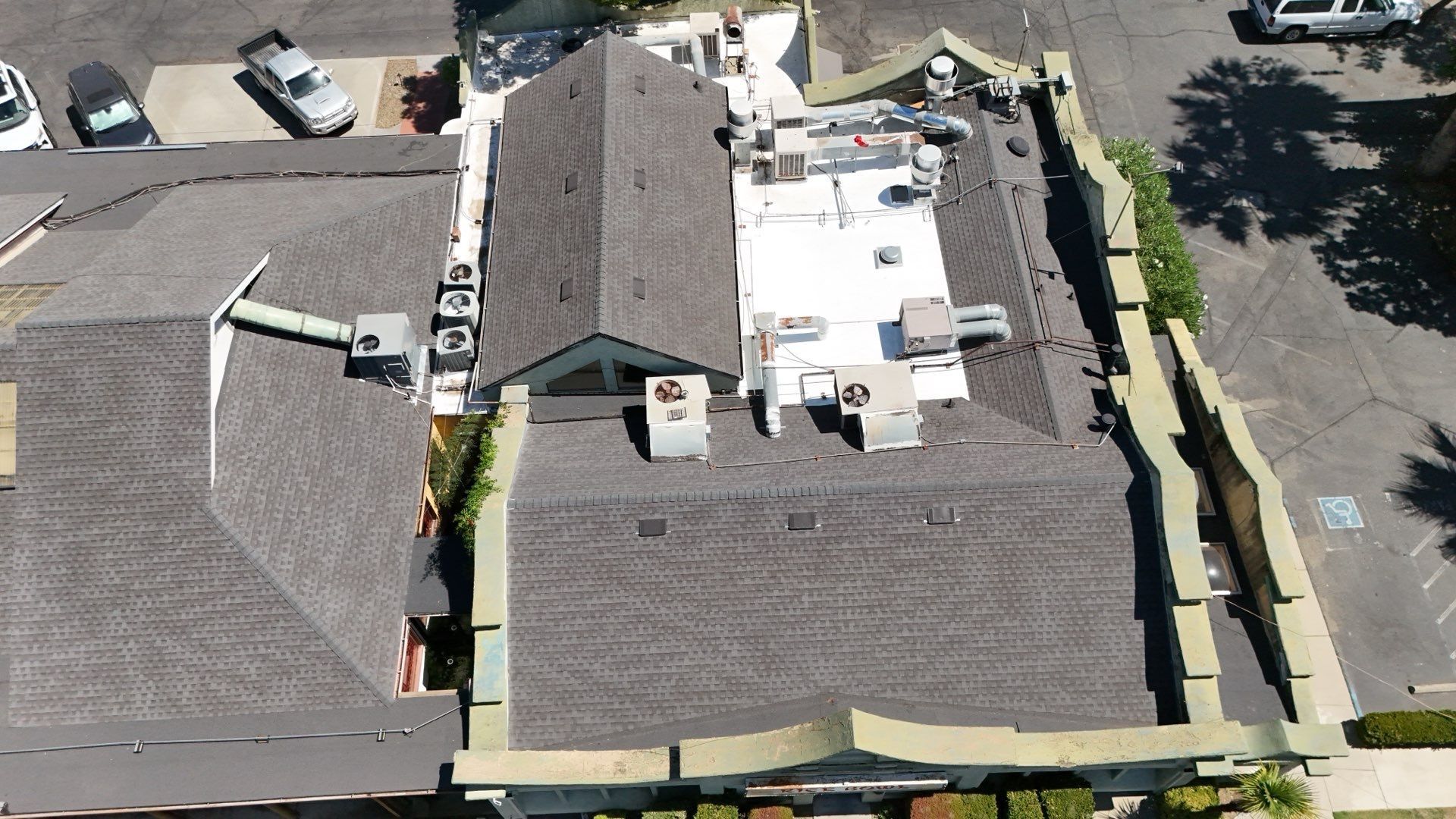 Aerial view of a building complex with gray roofs, rooftop equipment, and parking lots around it.