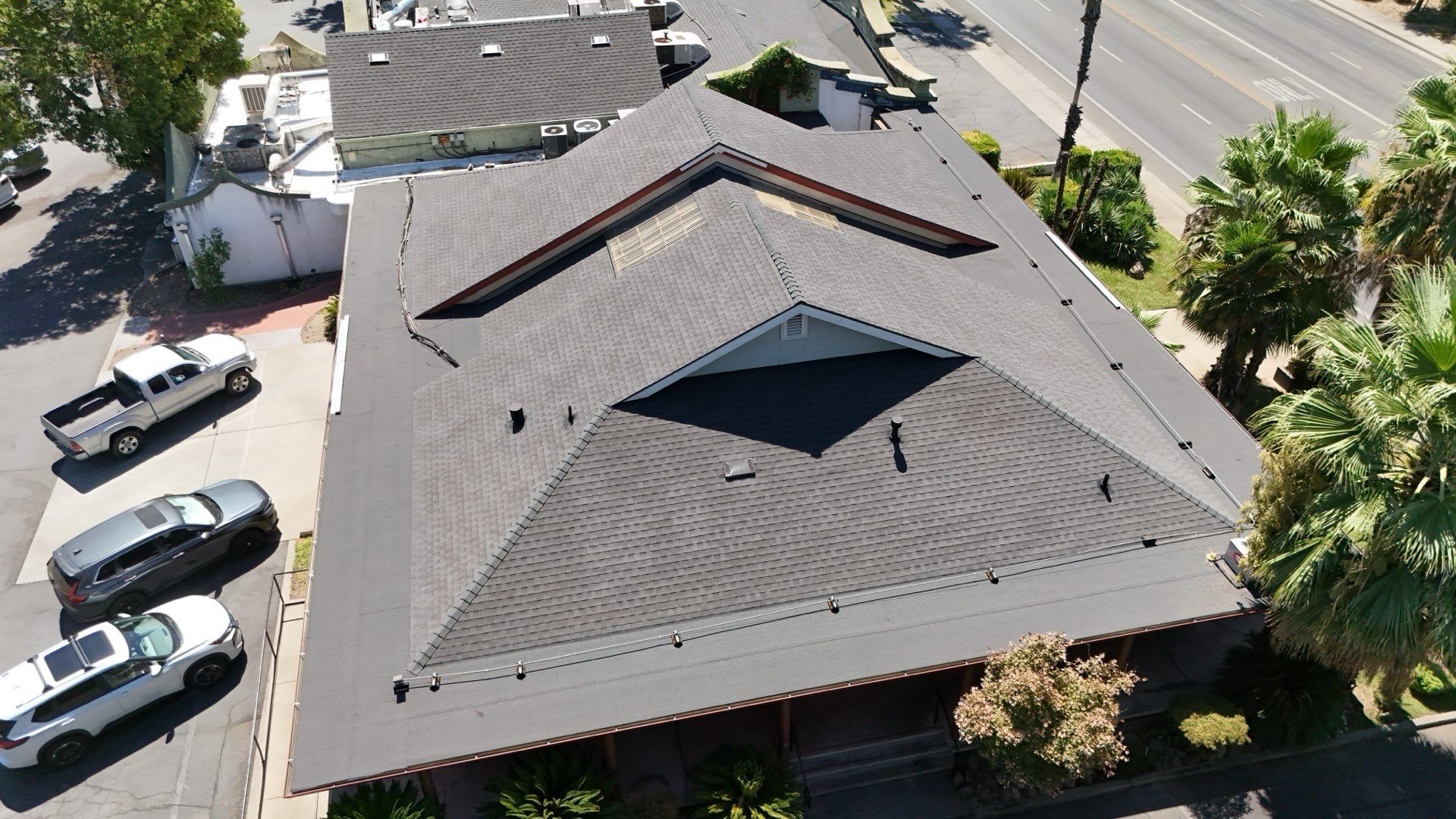 Aerial view of a gray-shingled house roof with a central skylight and parked cars nearby